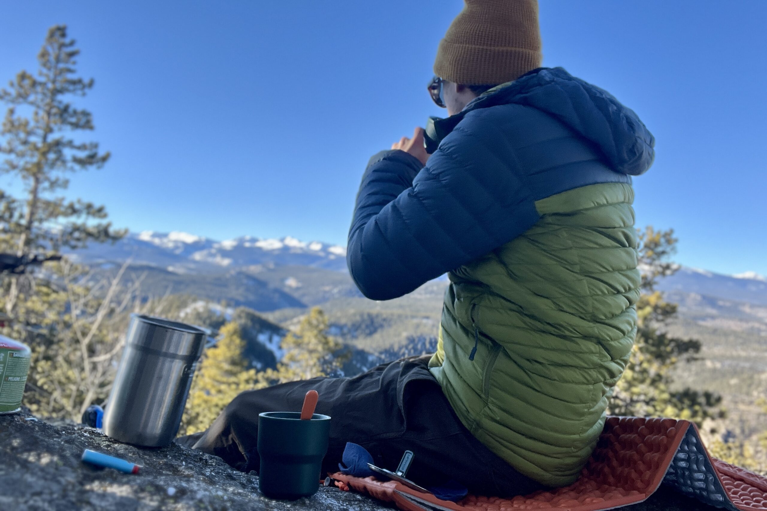 man drinking coffee in the morning with a nesting cup made by stanley while sitting on a rock ledge over a valley