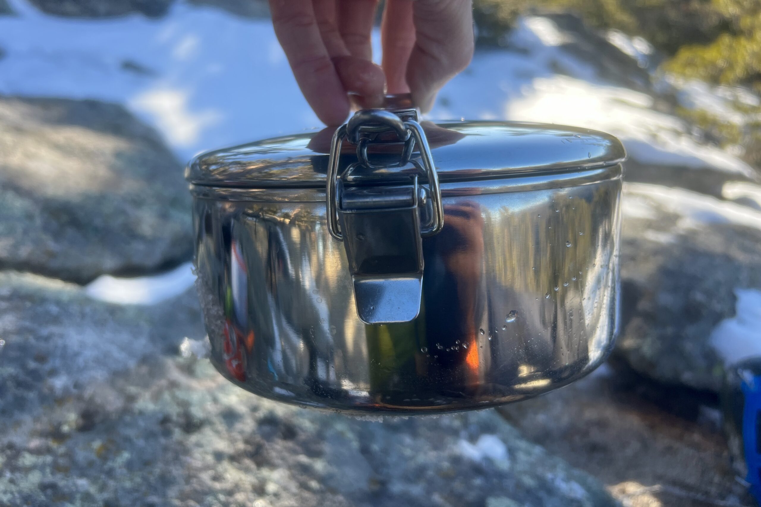 a hand holds a backpacking pot by the lid.