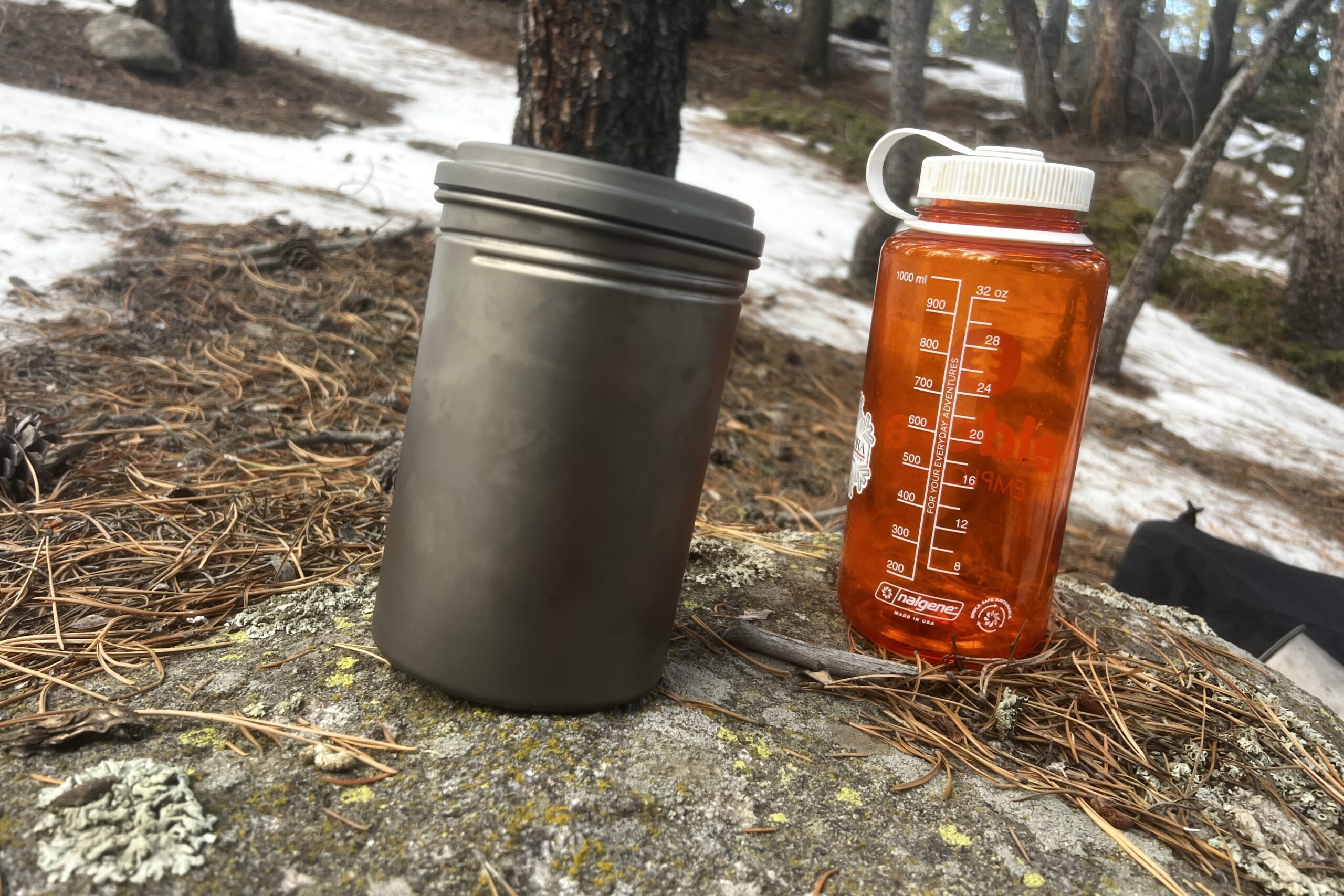 A titanium pot sits next to a nalgene bottle on a rock.