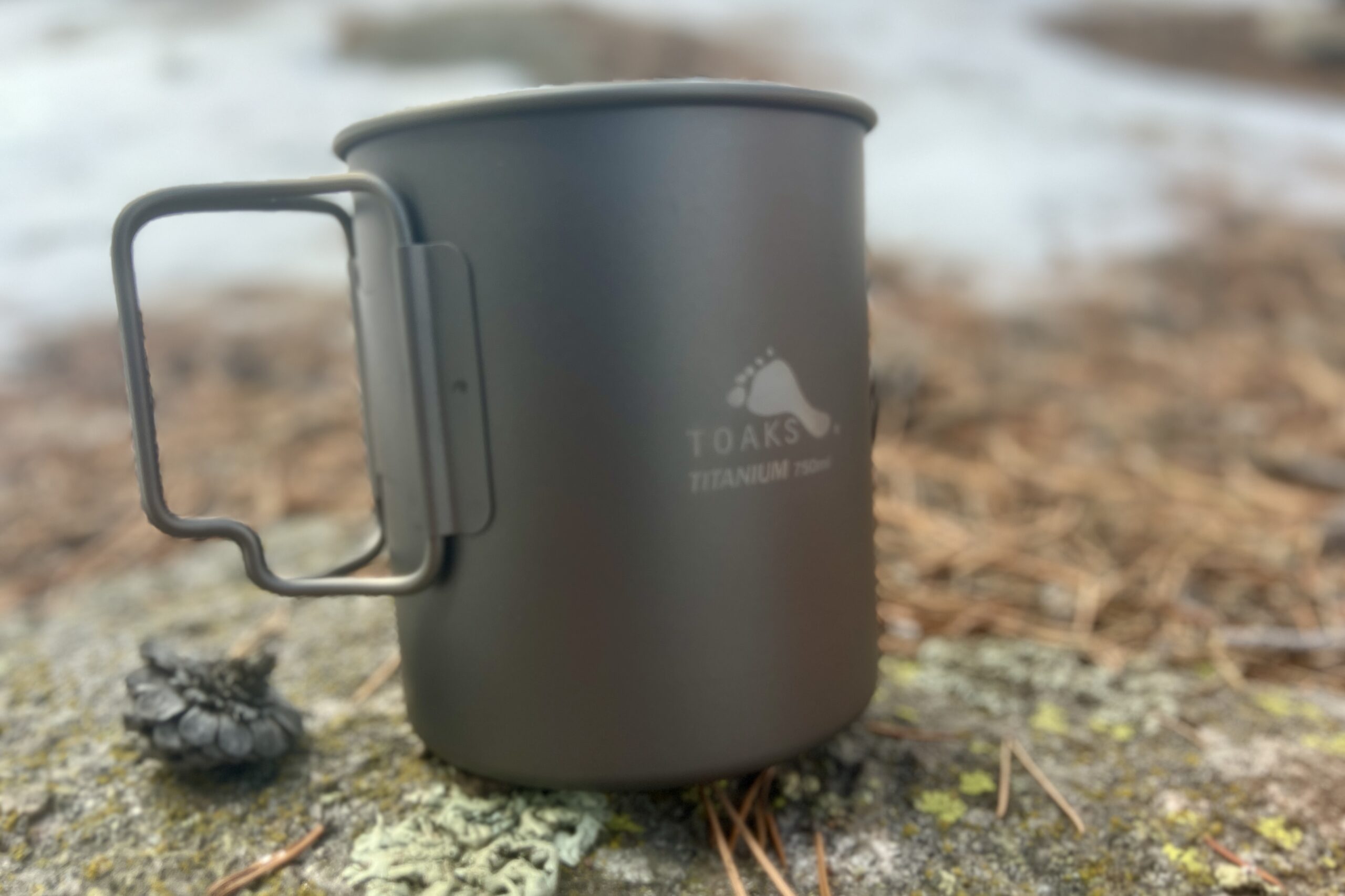A titanium cook pot sits on a rock.