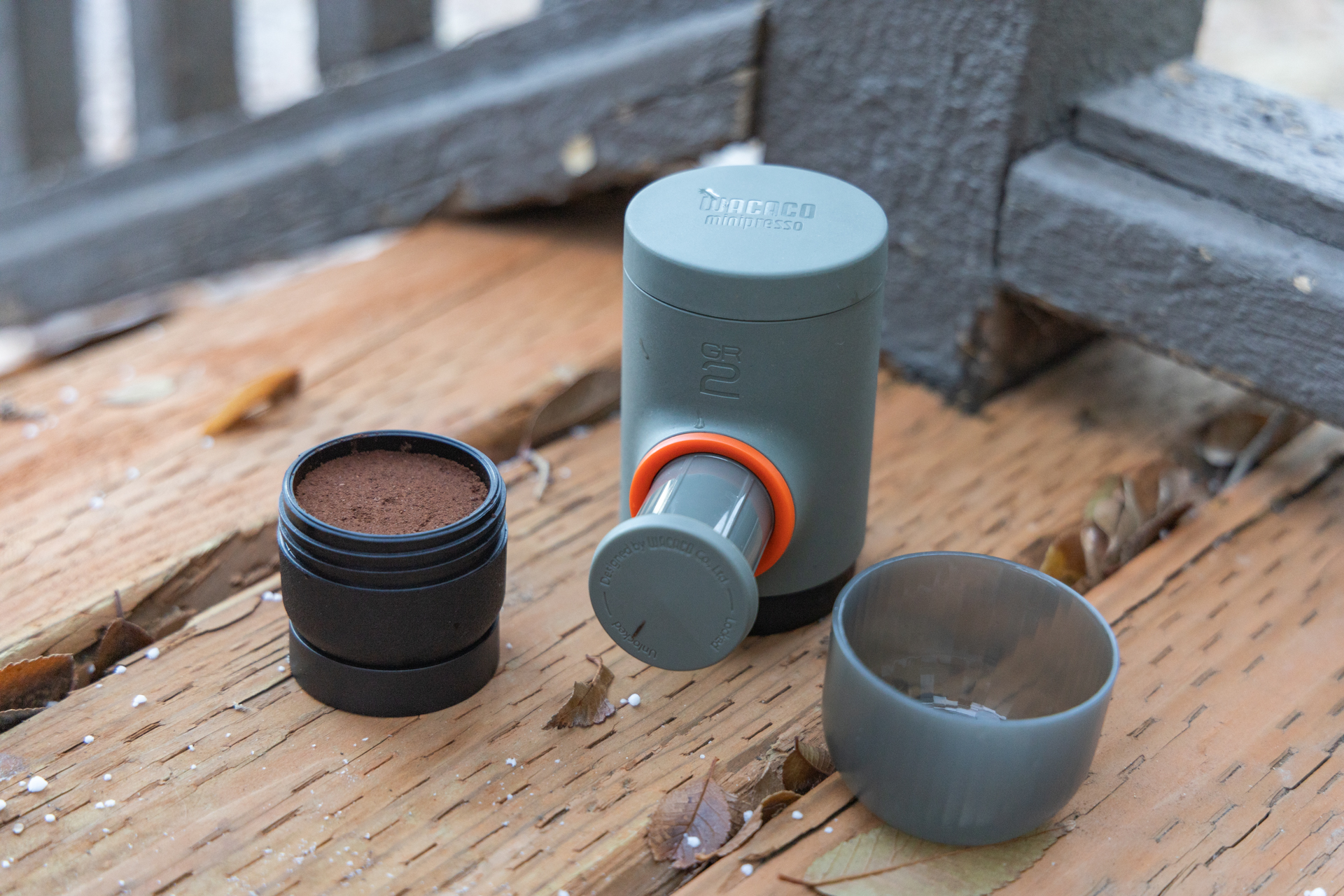 The Wacaco Minipresso disassembled and showing the basket filled with grounds, the cap that doubles as a cup, and the main body with pump extended.