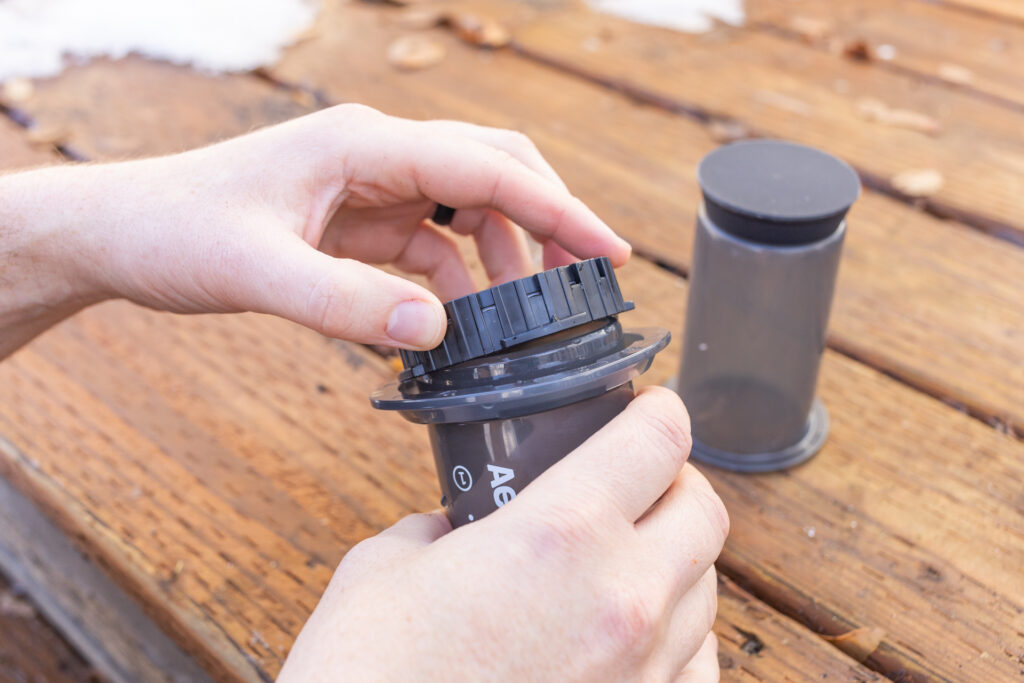 Hands screw the filter cap on an Aeropress Go.