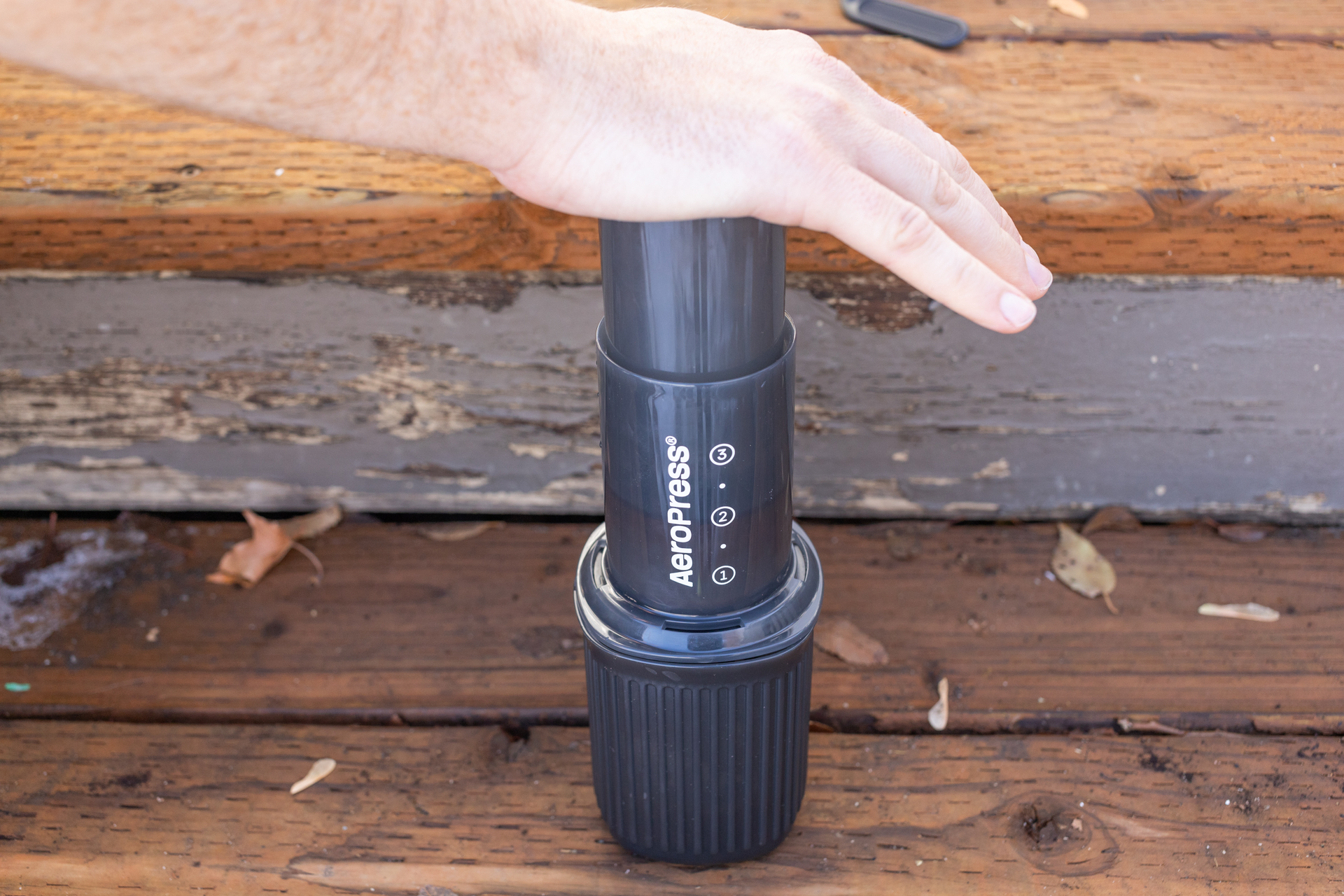 A hand presses an Aeropress Go plunger into the included cup.