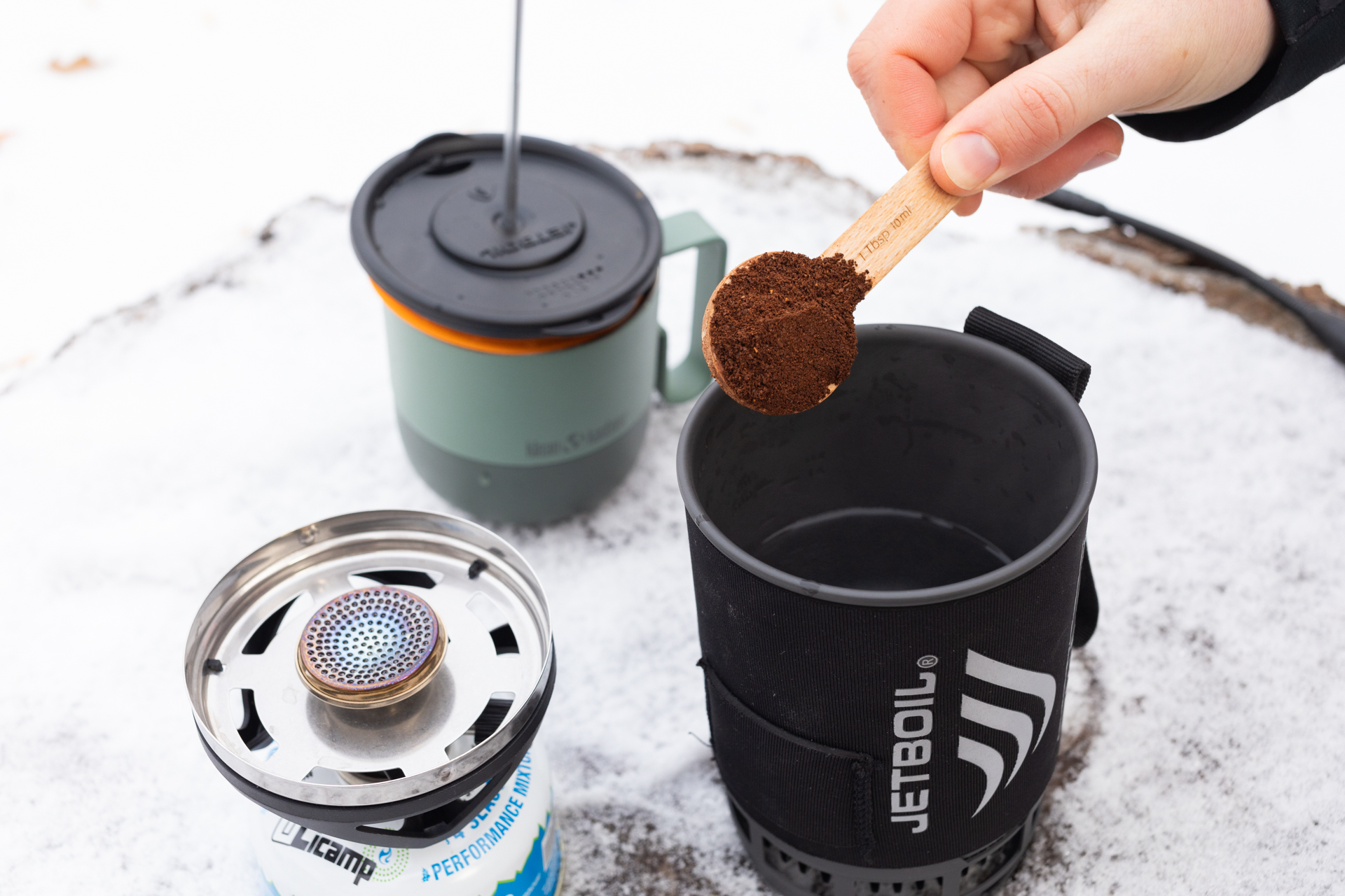 A hand scoops coffee in a Jetboil full of water.