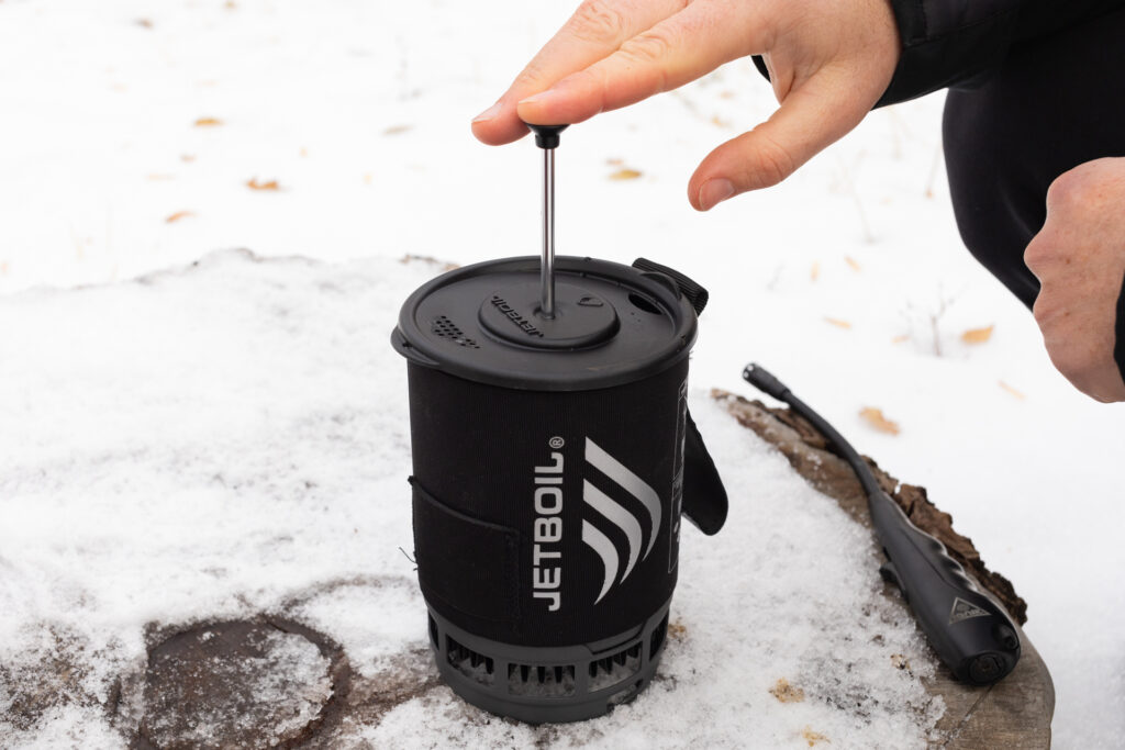 A hand presses the plunger of a Jetboil Silicone Coffee Press.