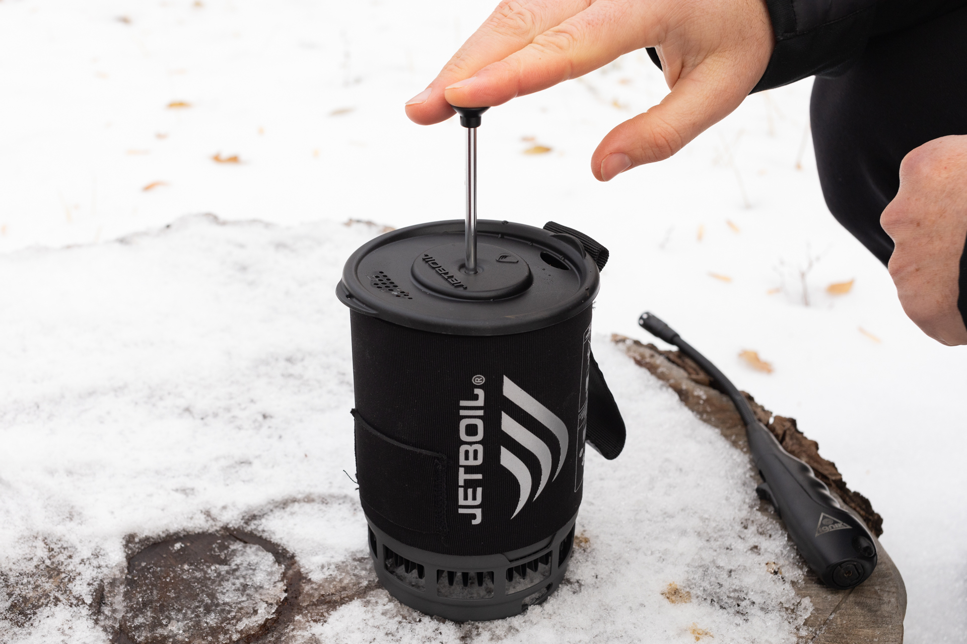 A hand presses the plunger of a Jetboil Silicone Coffee Press.