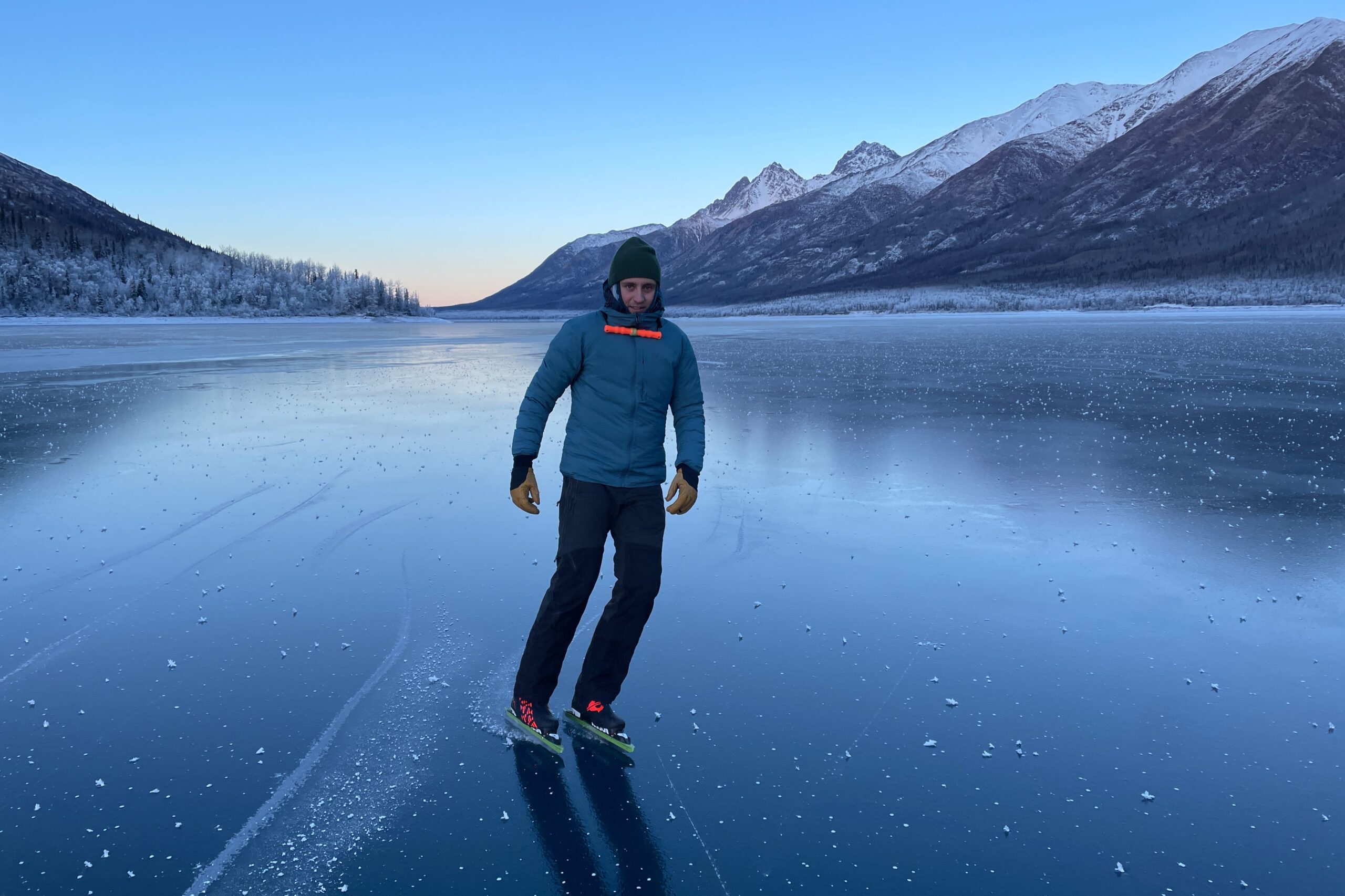 A man ice skates on a blue ice lake wearing a blue jacket.