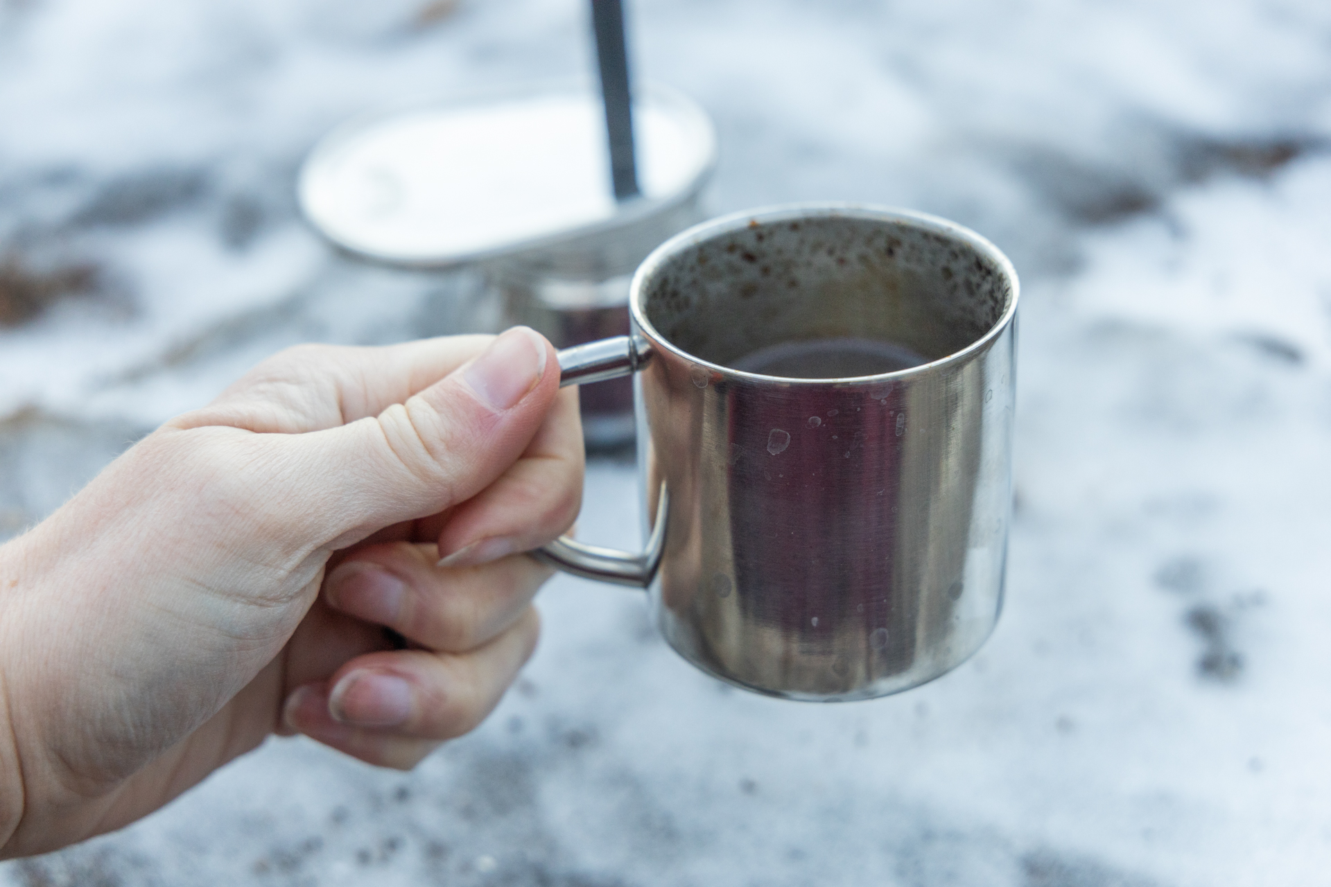 A hand holds the small cup full of coffee from next to the GSI Mini Espresso.