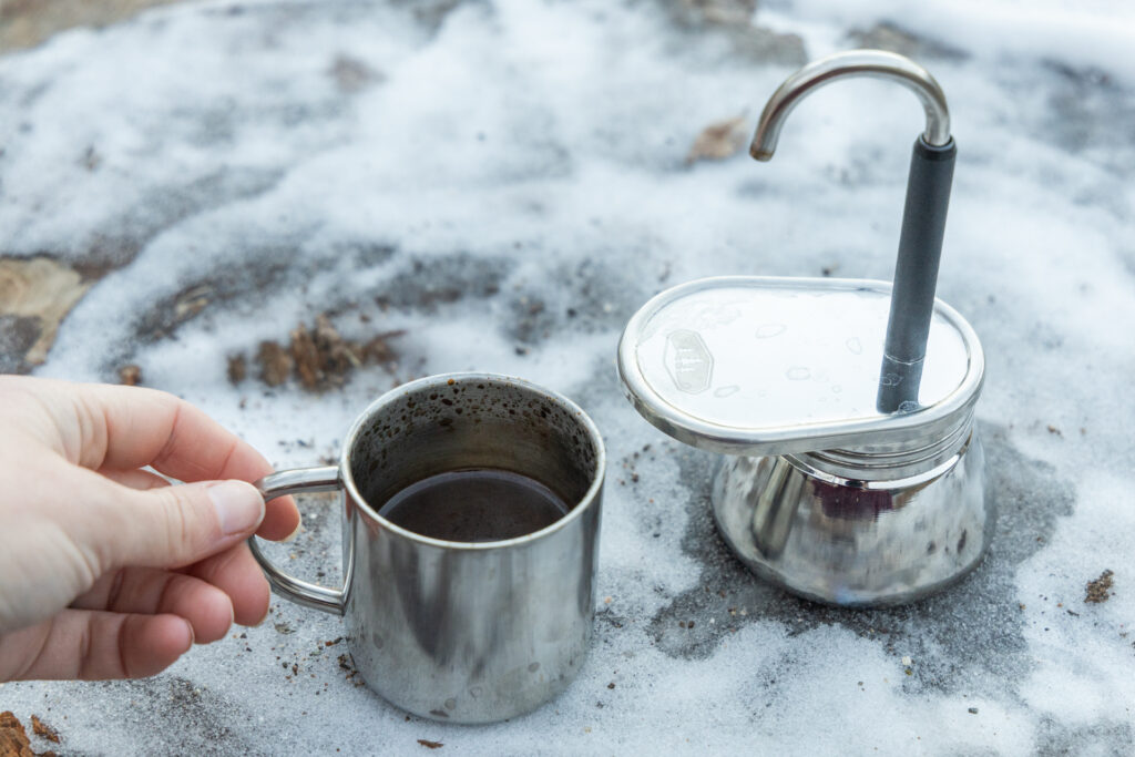 A hand grabs the small cup full of coffee from next to the GSI Mini Espresso.