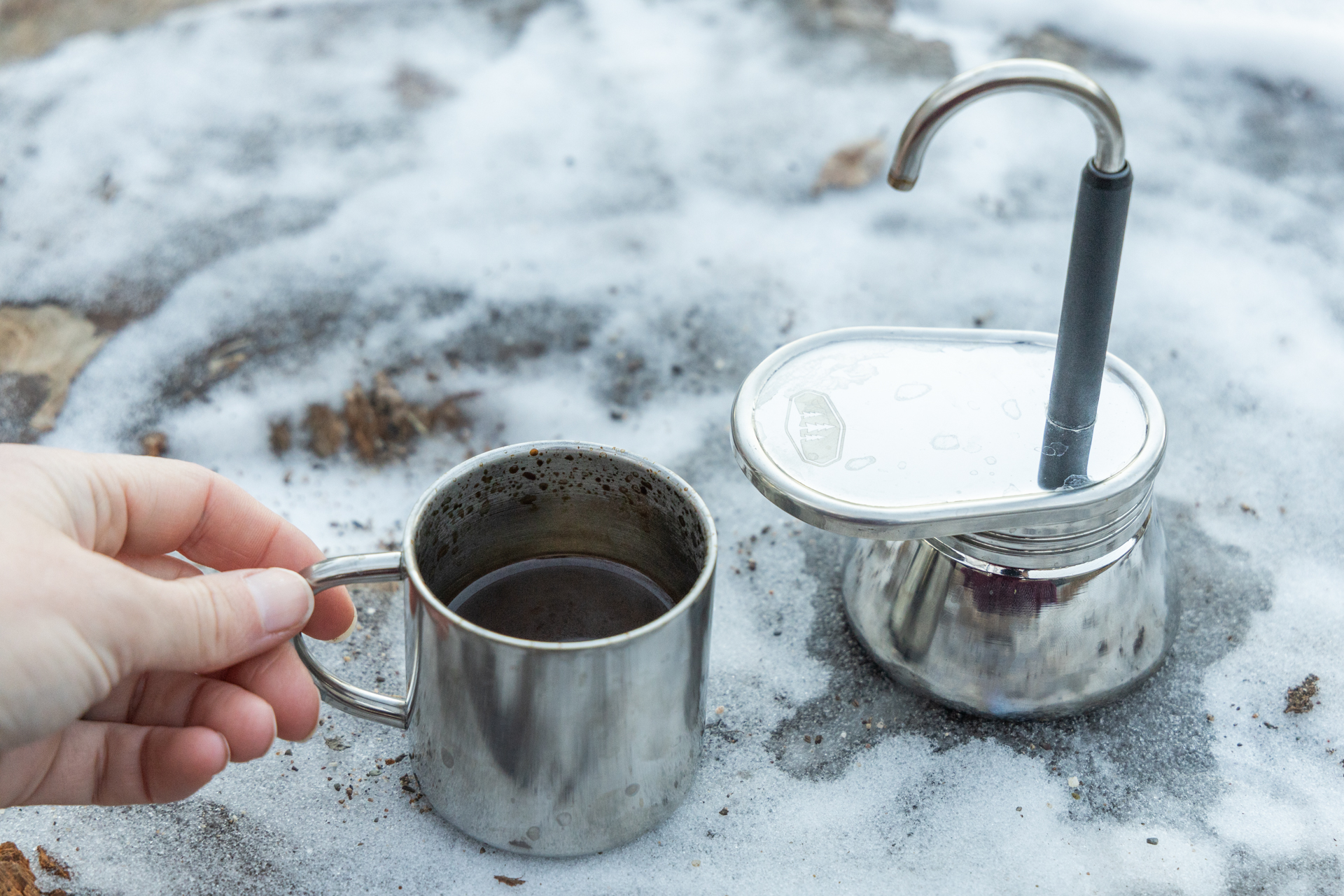 A hand grabs the small cup full of coffee from next to the GSI Mini Espresso.