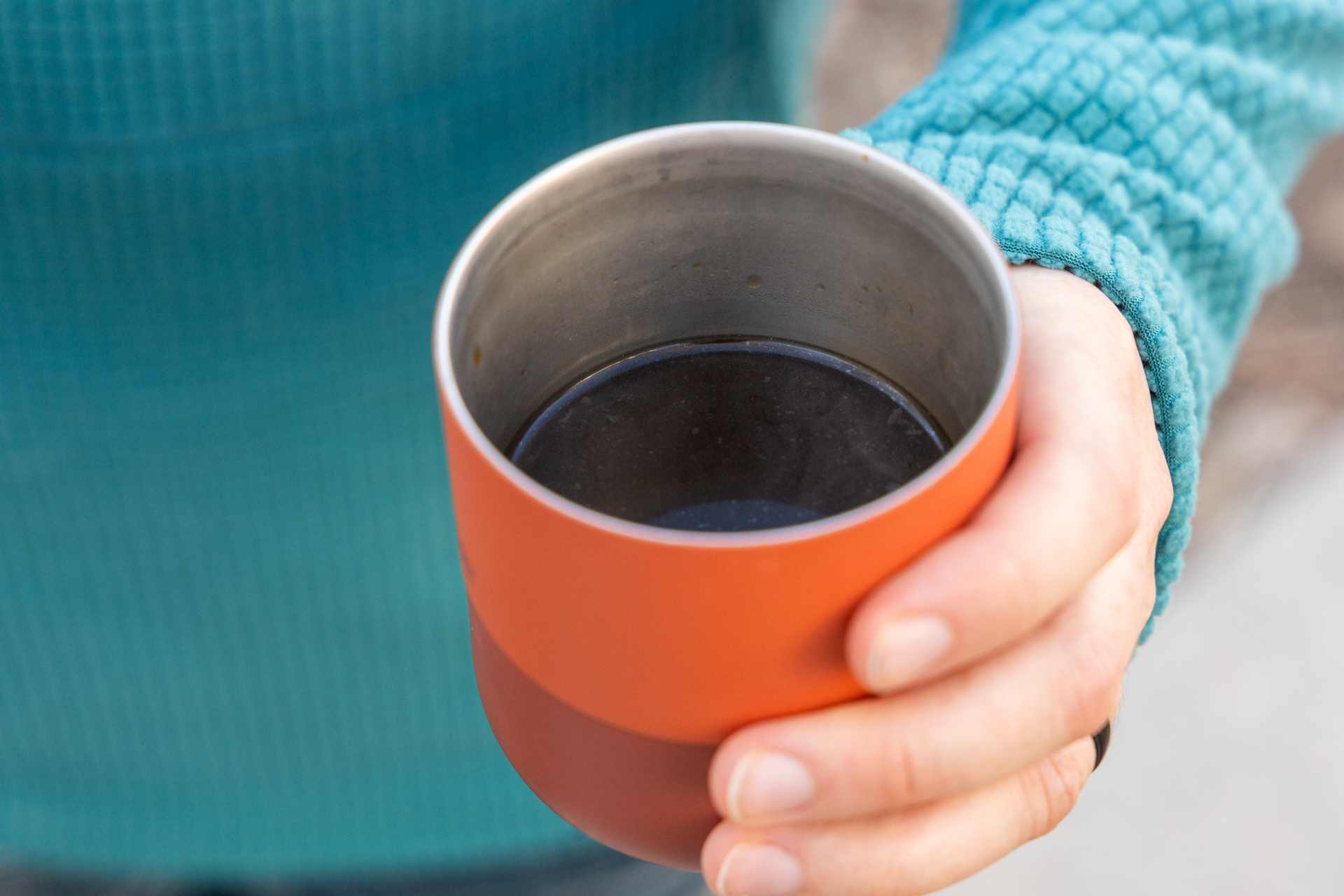 A hand holds a mug of dark coffee.