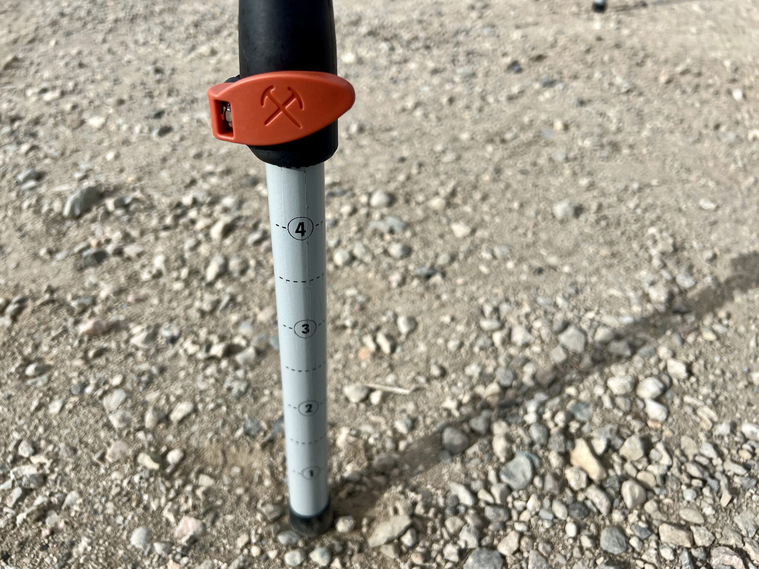 Close-up of the REI Camp Prep Table's adjustable legs. It has an orange lever lock. The leg is standing on gravel.
