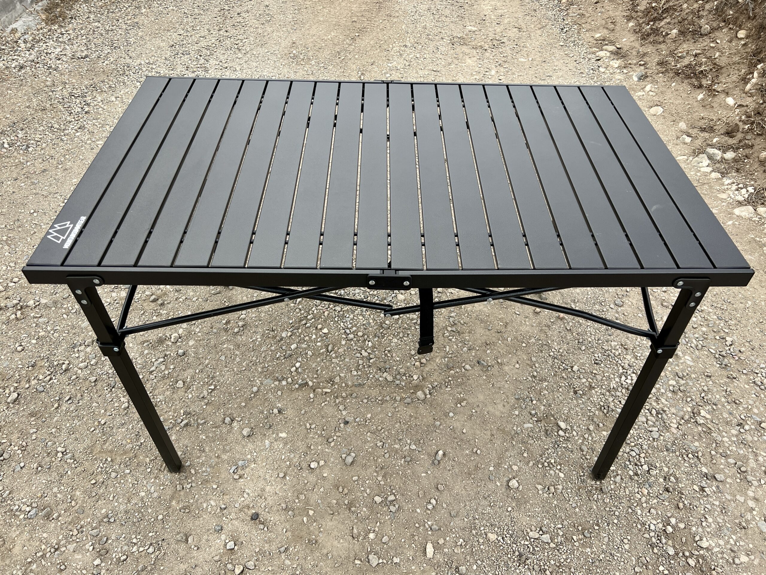 The Mountain Summit Gear Heavy Duty Roll Top Table stands on gravel.