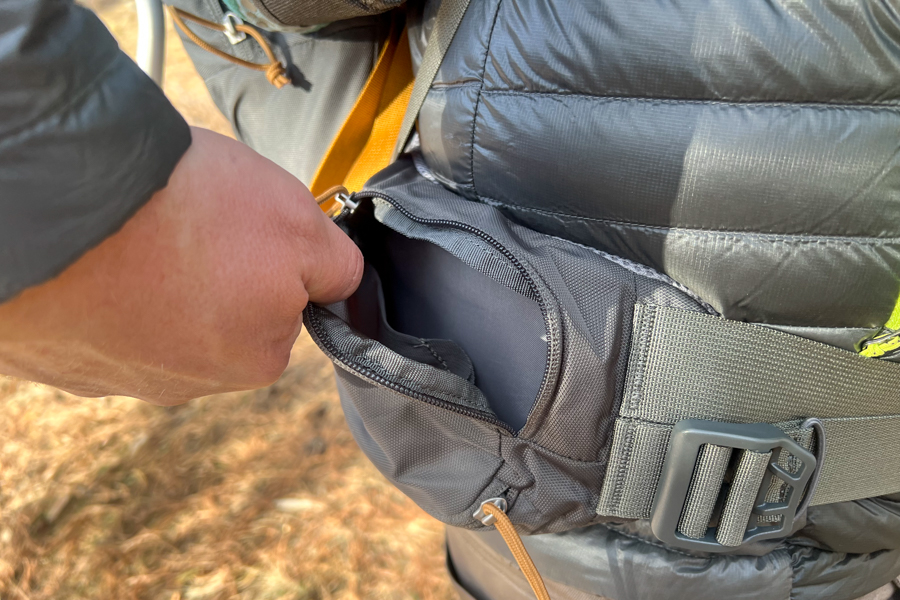 Close-up of a hand opening the hip belt pocket on the Kelty PerfectFIT Journey Elite carrier.