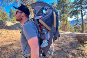 A close-up of a child's foot secured in a stirrup strap of a baby backpack carrier, providing support and comfort during hikes.