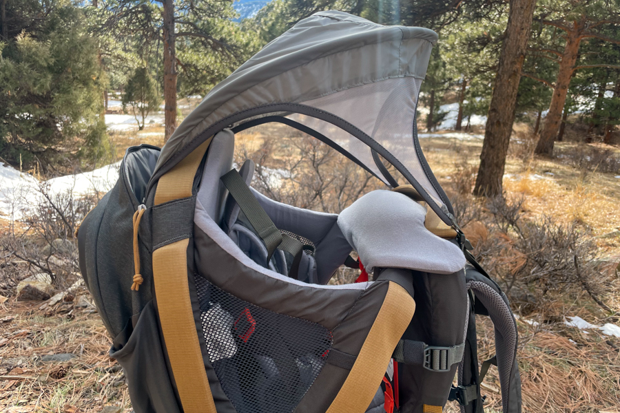 Side view of the Kelty PerfectFIT Journey Elite with the sunshade extended in a forest setting.