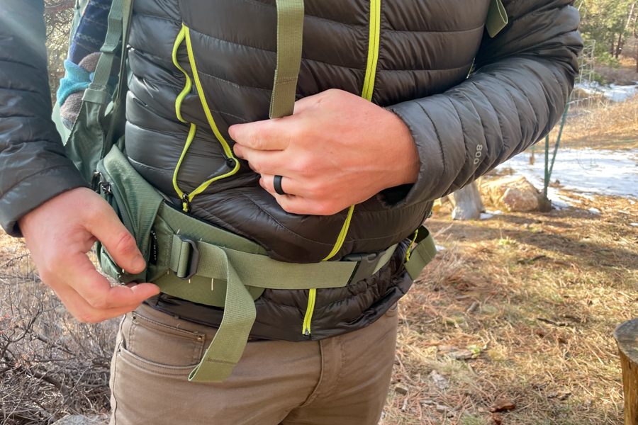 A user adjusting the waist belt of the Osprey Poco Premium for a snug and secure fit.