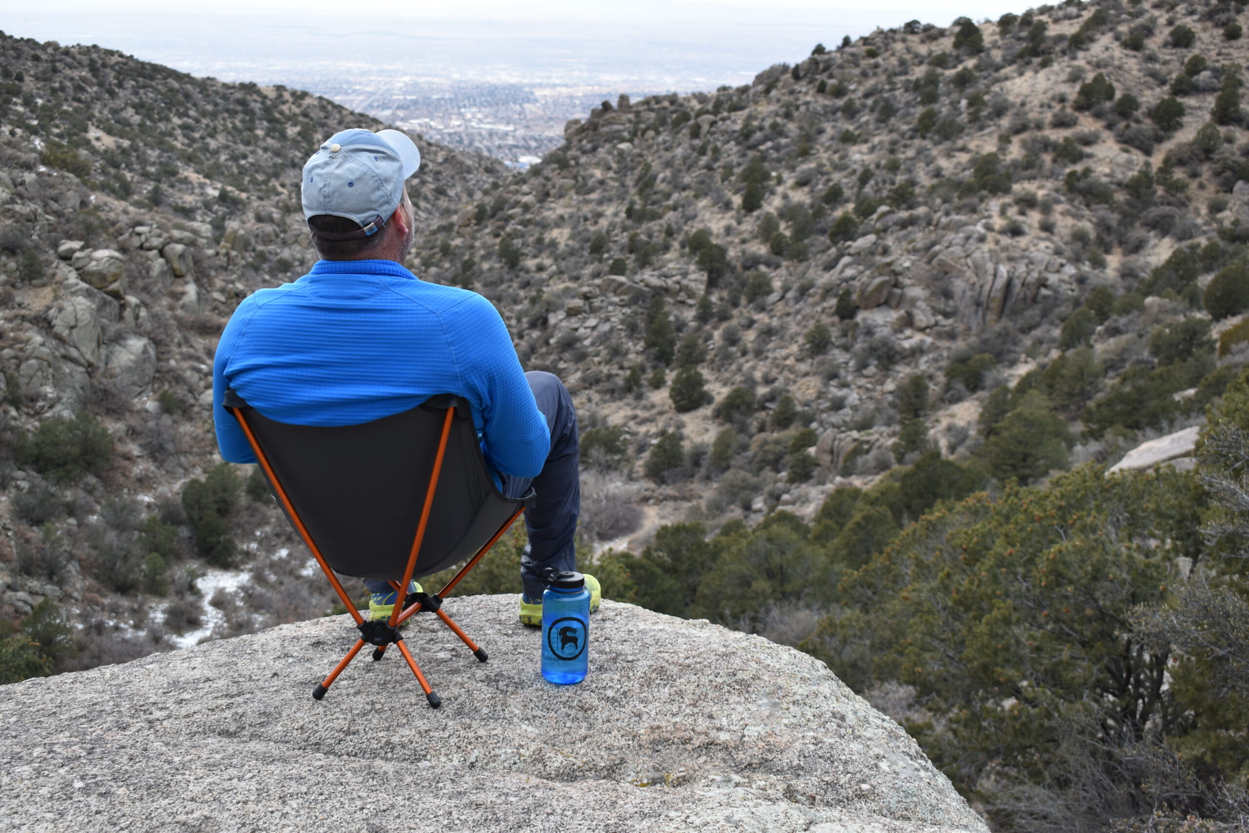 View from the back of a man sitting on the Flexlite Air Chair on a cliff looking down a desert valley