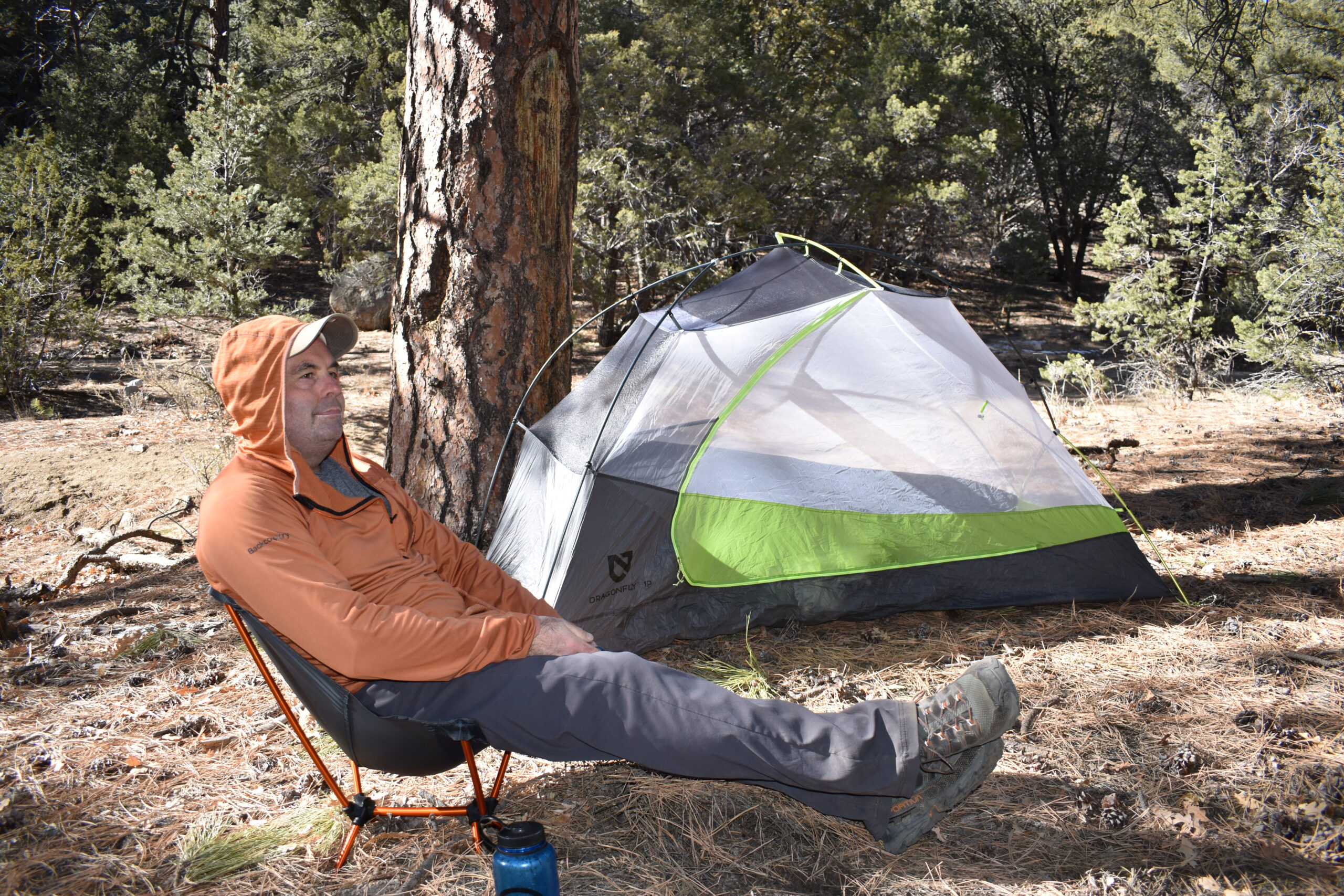 Male camper relaxes at a campsite in the pines with his legs stretched out