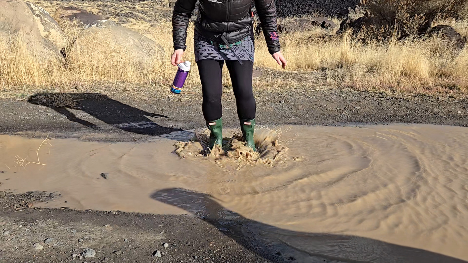 a woman up to her ankles in muddy water wearing the hunter original short rain boot