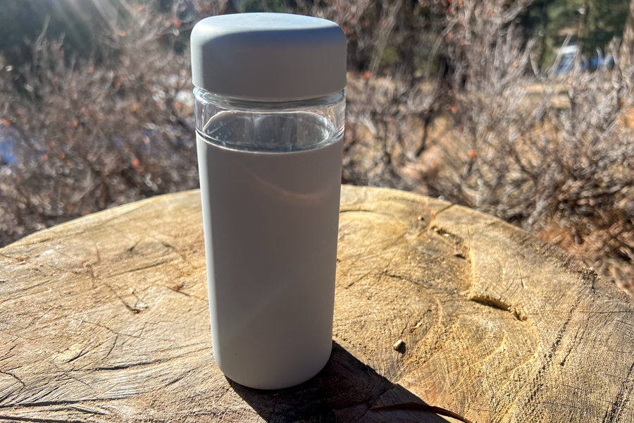 A sleek white Porter Bottle sitting on a wooden stump outdoors, framed by natural surroundings.