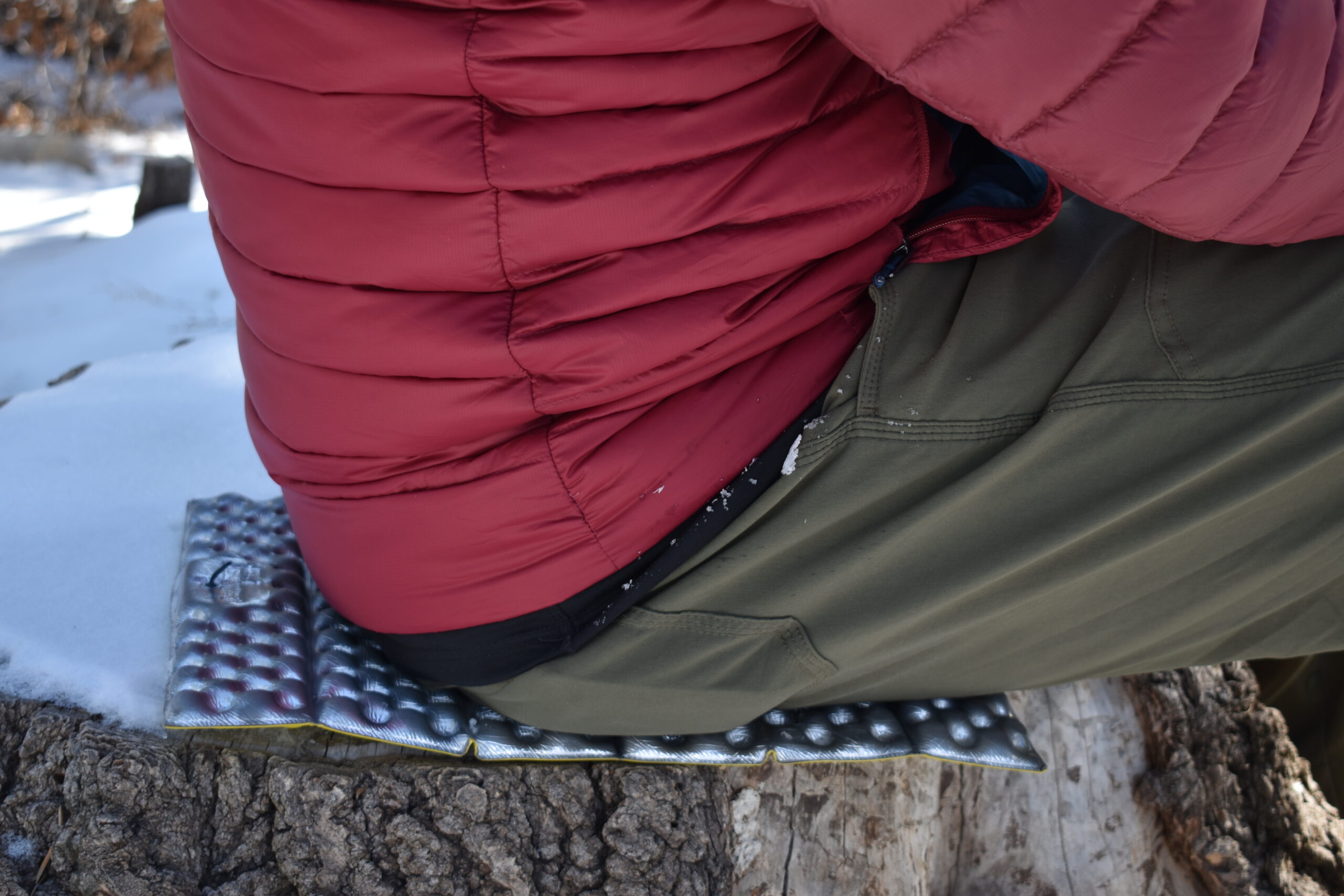 Close up of a backpacker siting on a foam pad on a snowy stump