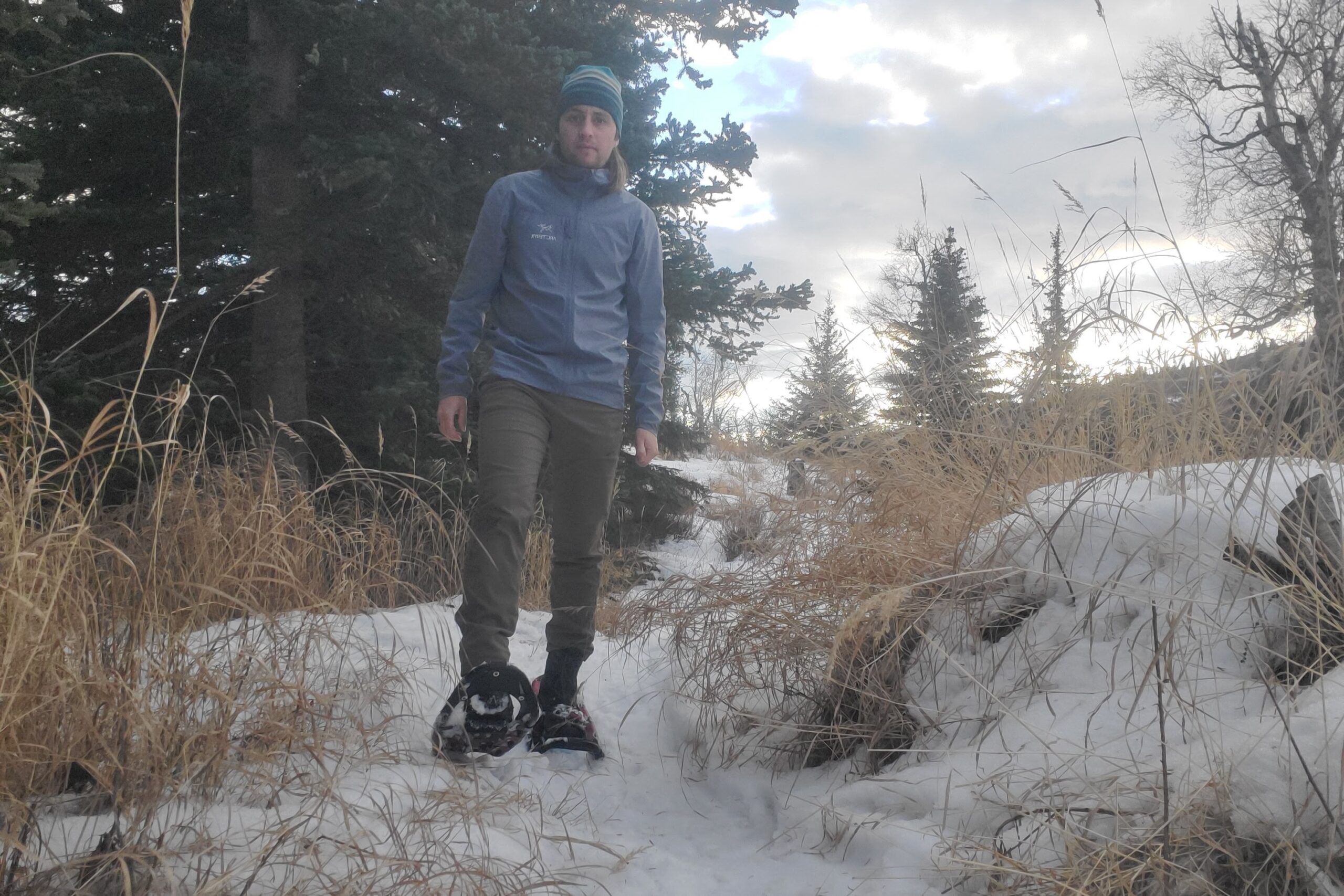 A man snowshoes down a trail with yellow grass on the edges.