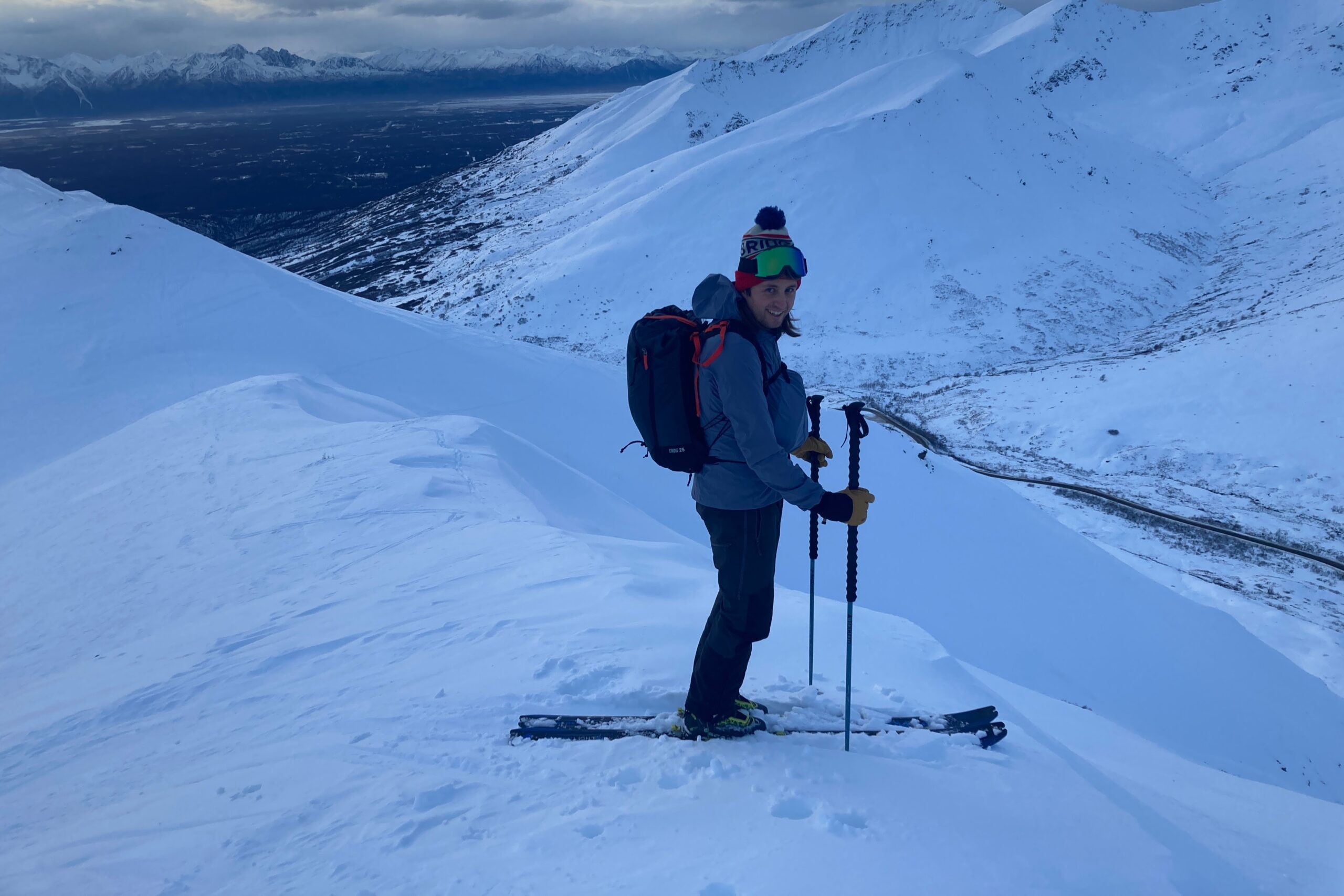 A man stands on a winter ridgeline wearing skis.