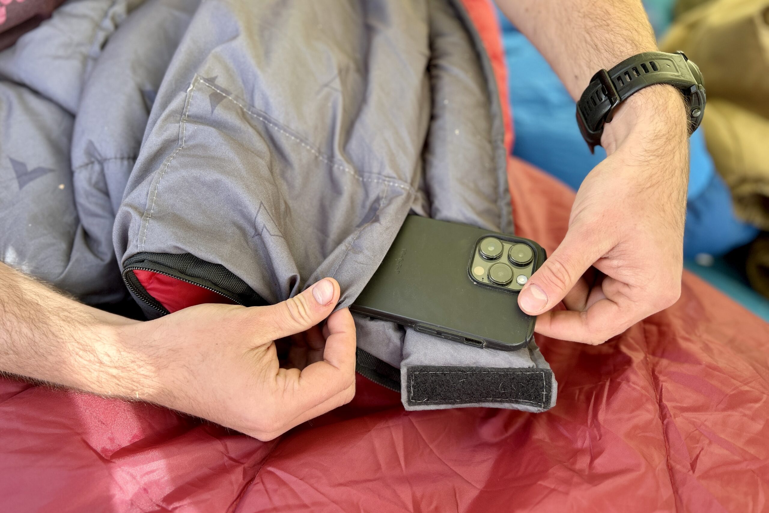 Close-up image of a person pulling a phone out of an internal stash pocket of a sleeping bag.