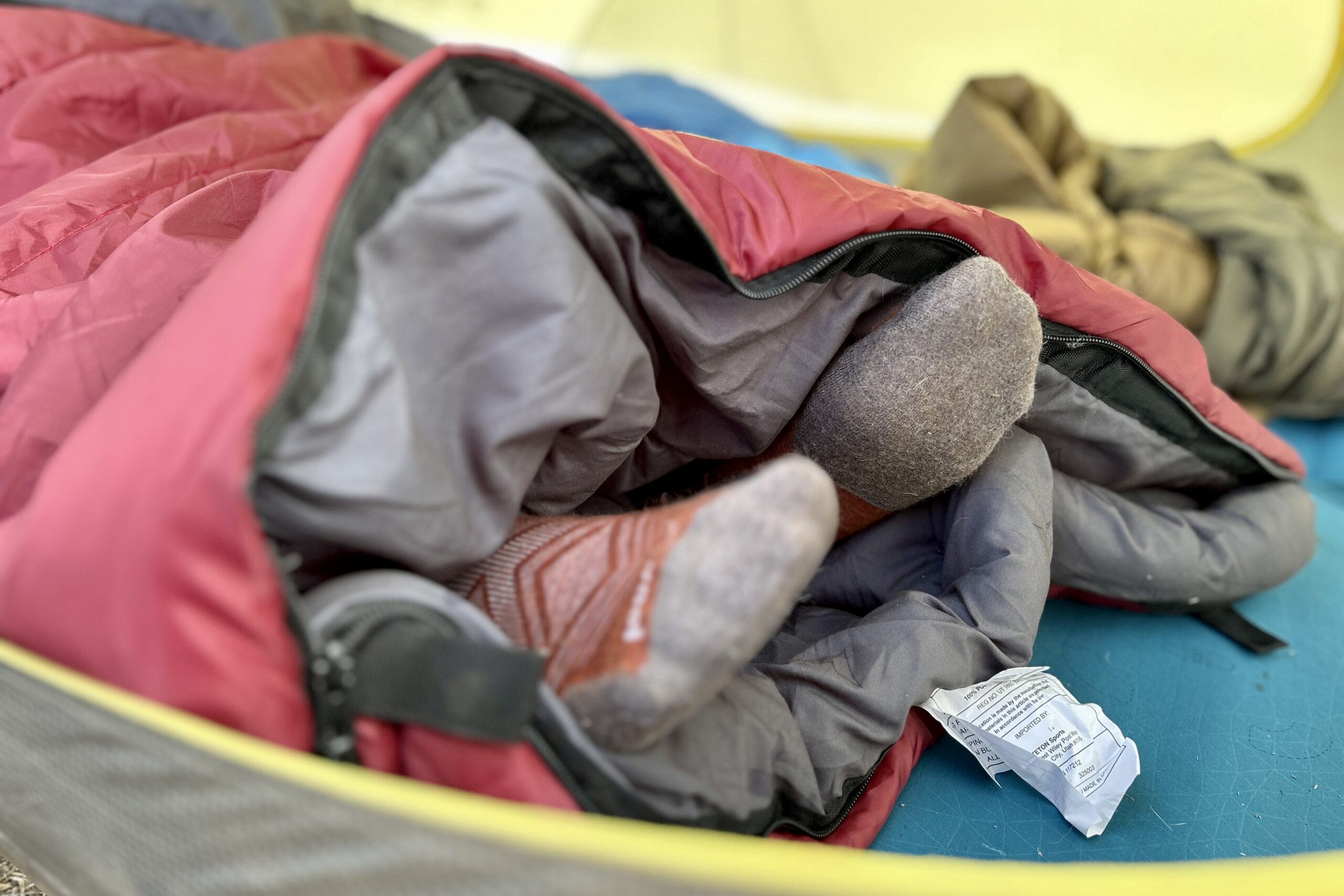 Close-up image of two feet sticking out of the unzipped bottom of a sleeping bag.
