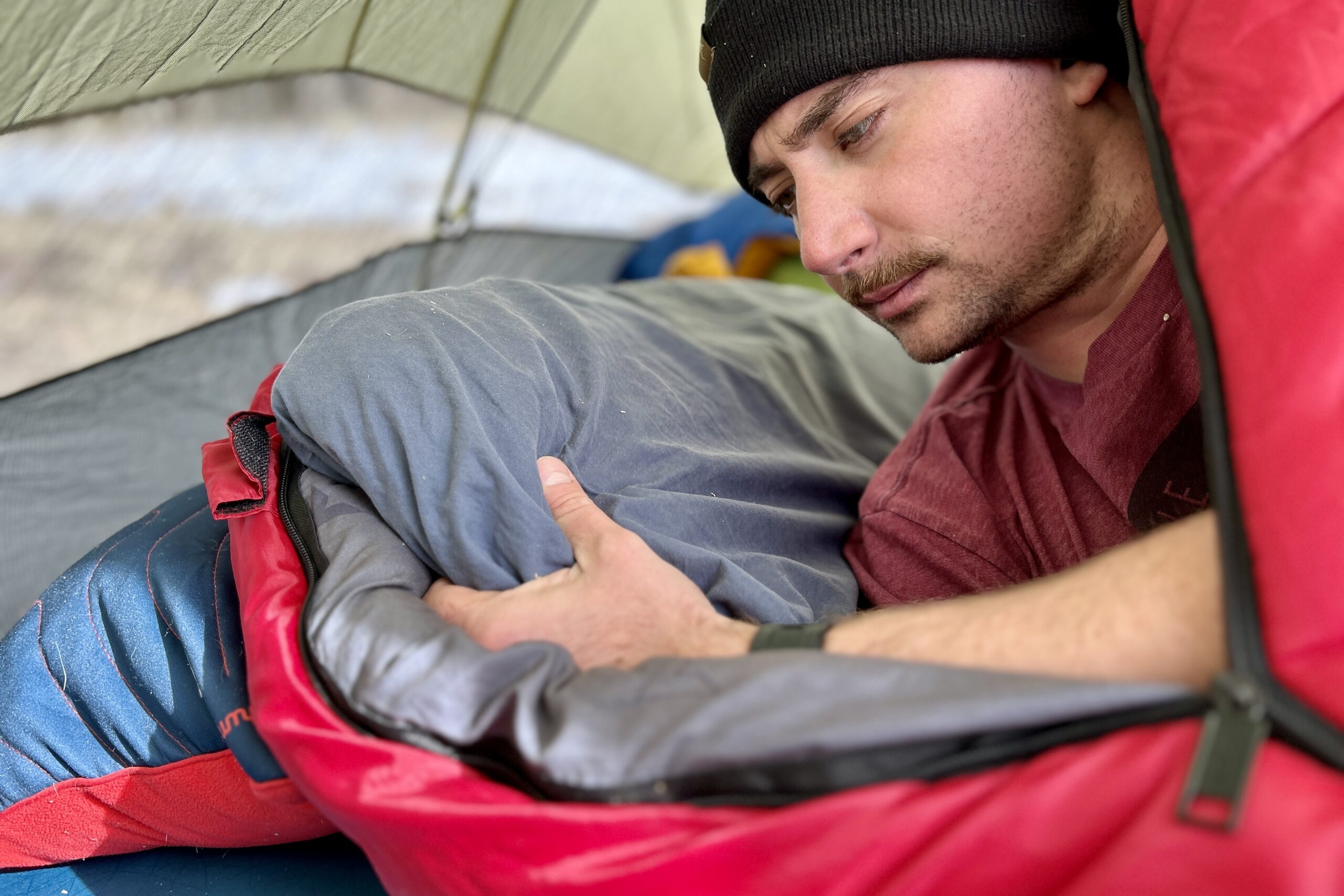 Close-up image of a man adjusting a pillow while inside a sleeping bag.