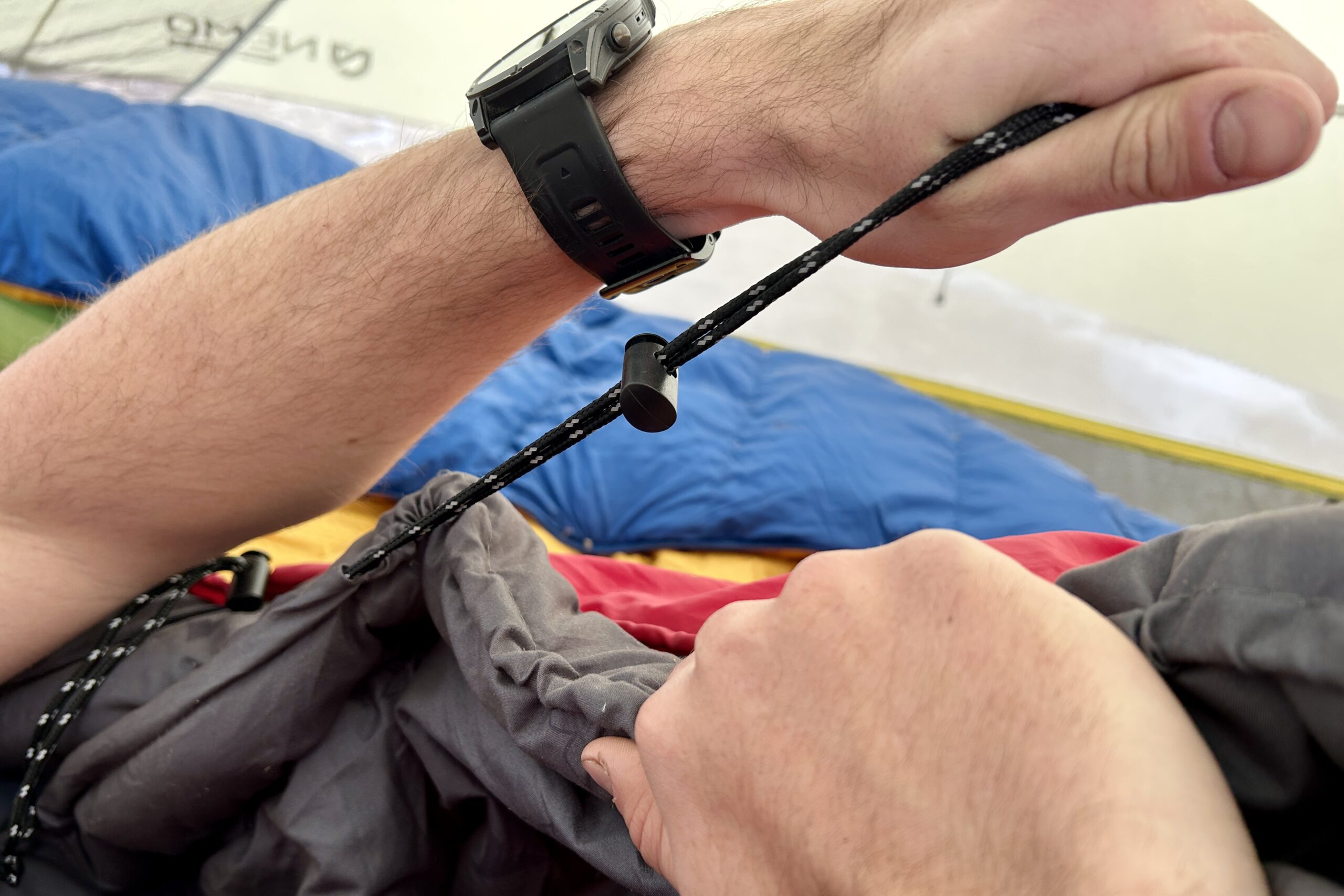 Close-up image of a person tightening the cinch cord on the top of a sleeping bag.