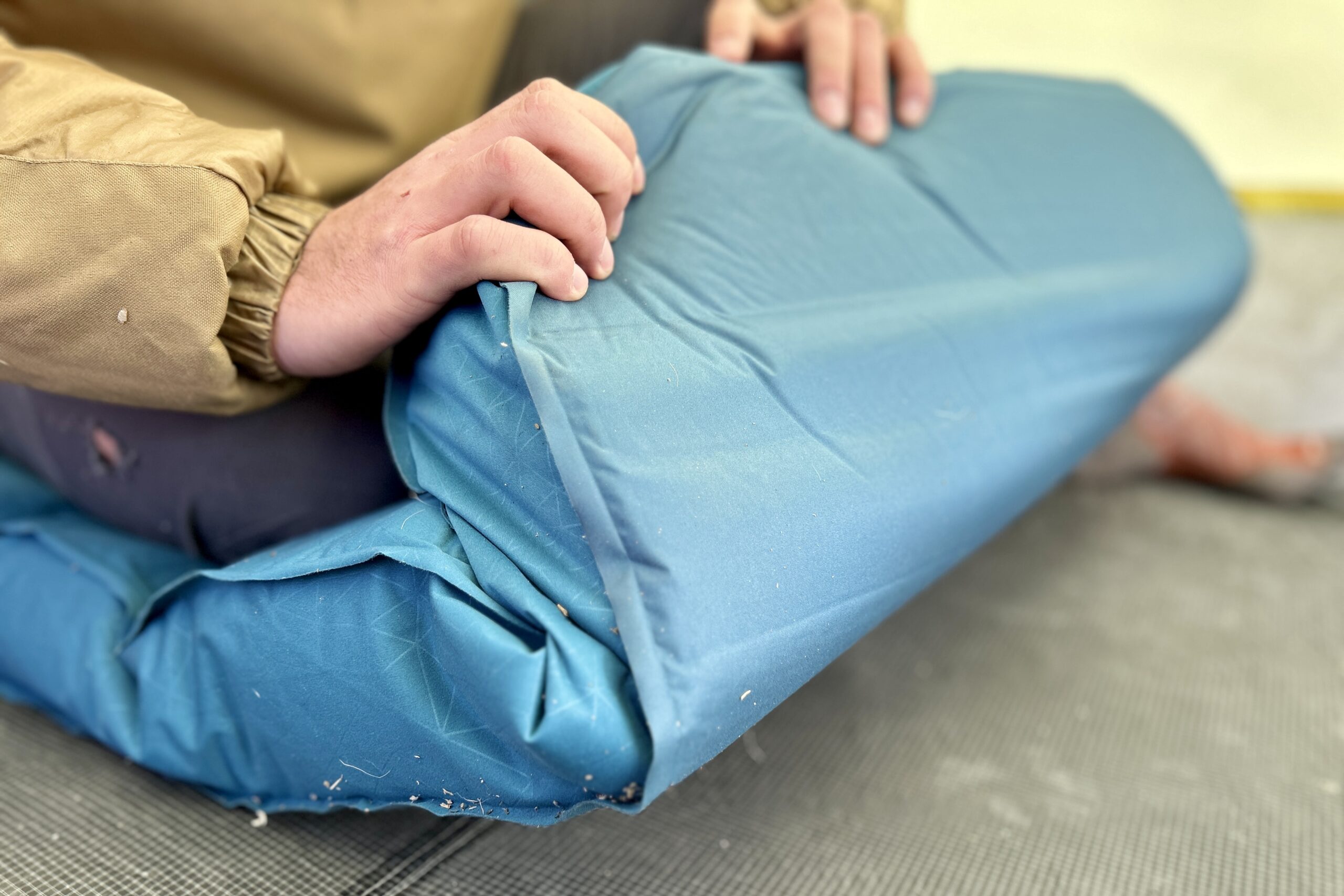 Close-up image of two hands folding the end of a thick camping mattress inside a tent.