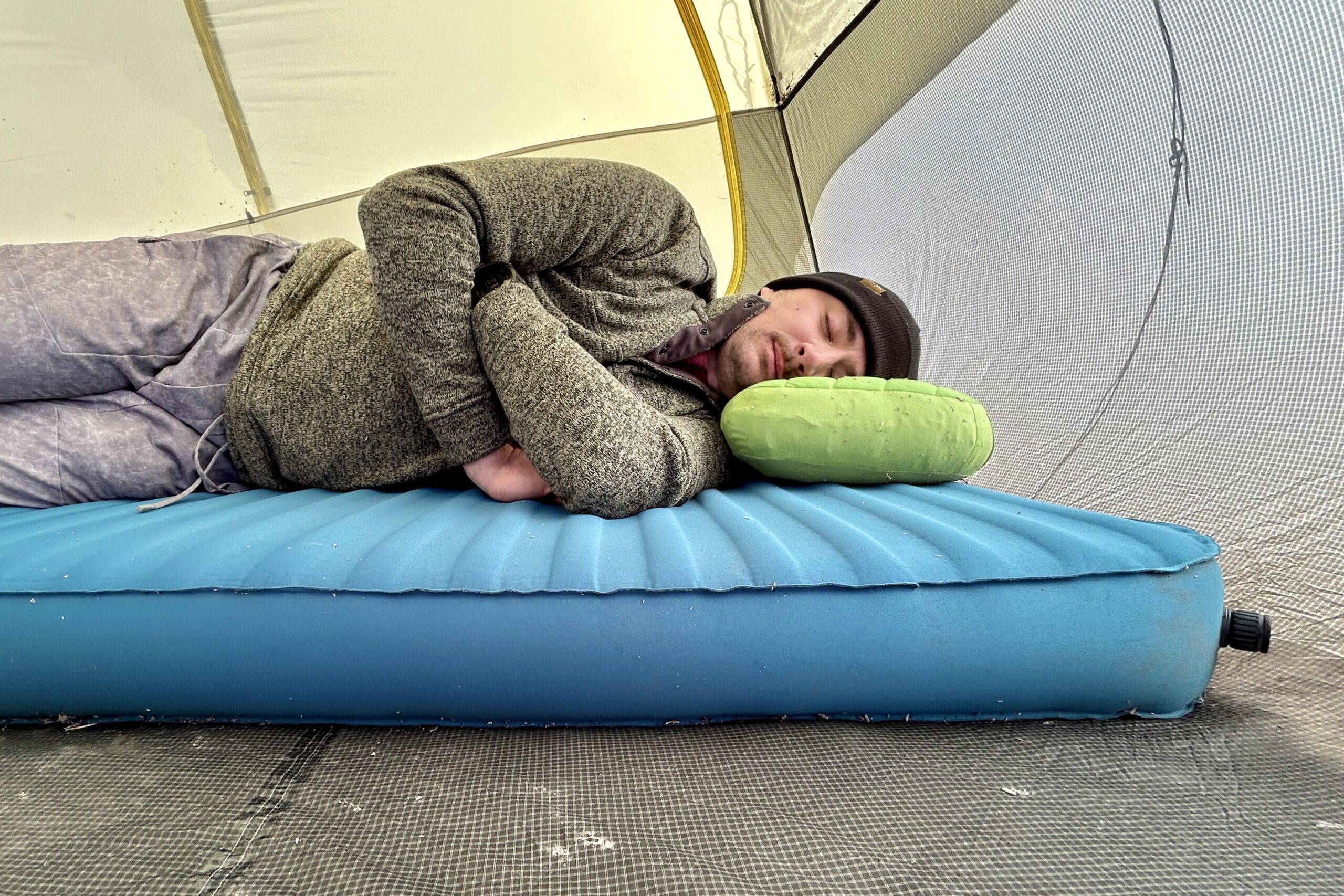 A man rests on a camping mattress with a backpacking pillow in a tent.