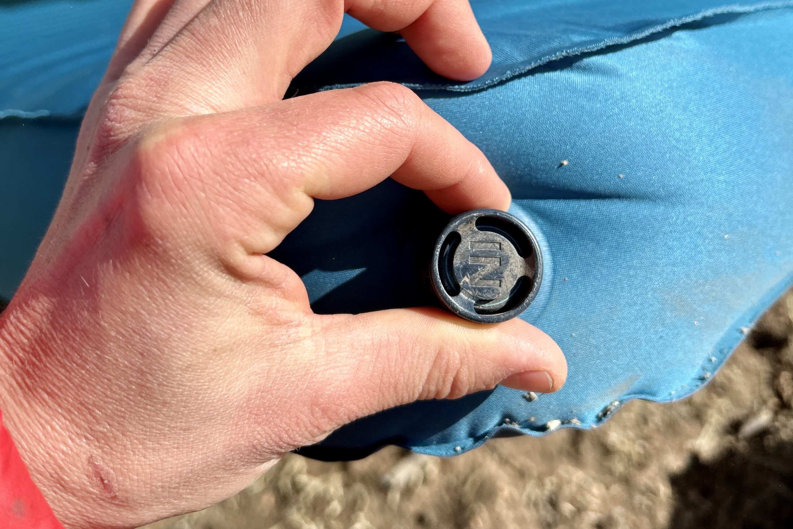 Close-up image of the air intake knob on a sleeping mattress with a person's hand on it, showing how it twists.