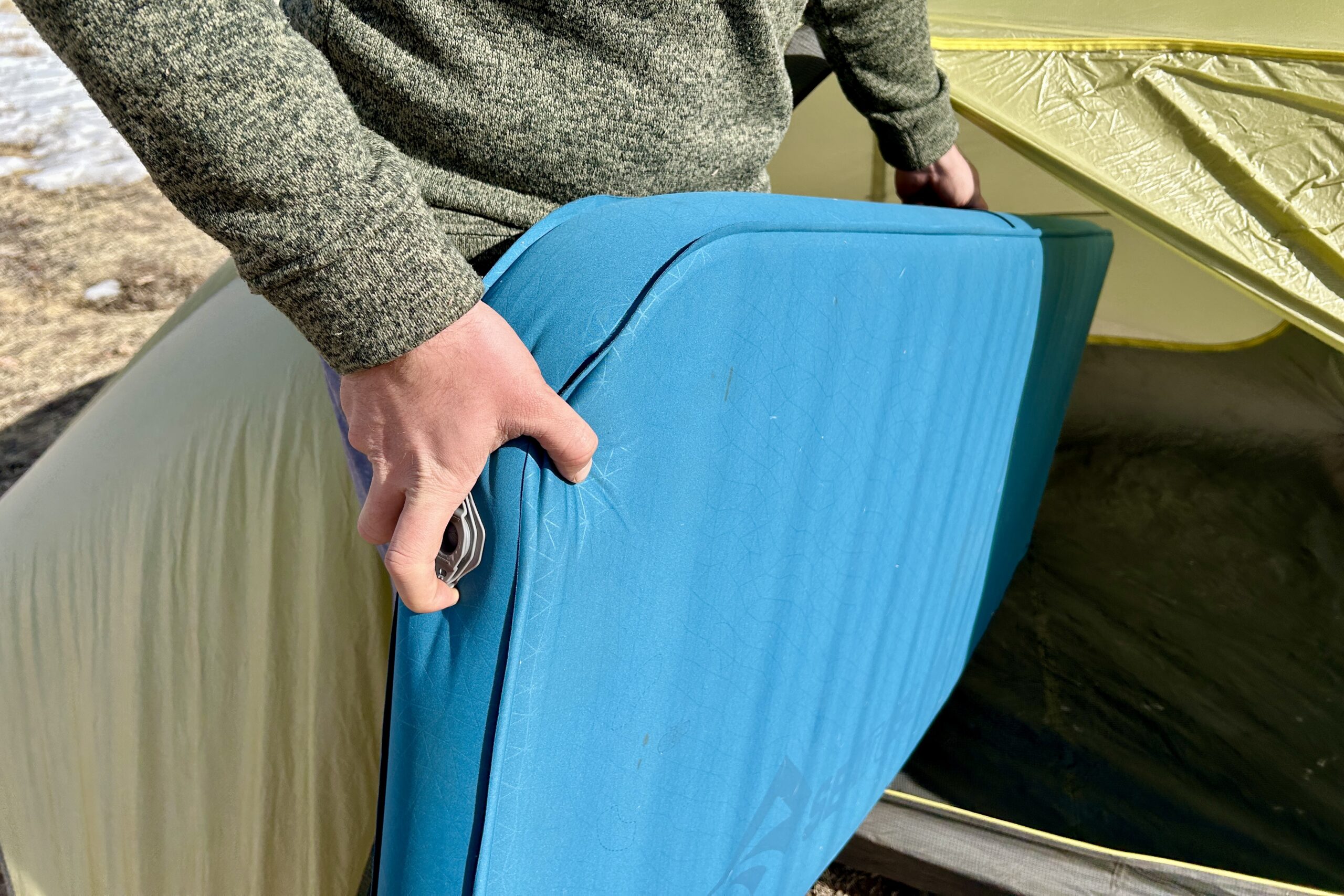 Close-up image of a person putting a camping mattress into a tent.