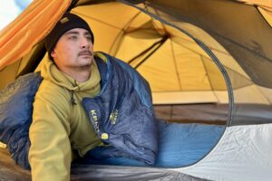 A man looks out of a tent to take in the view while still in his sleeping bag.