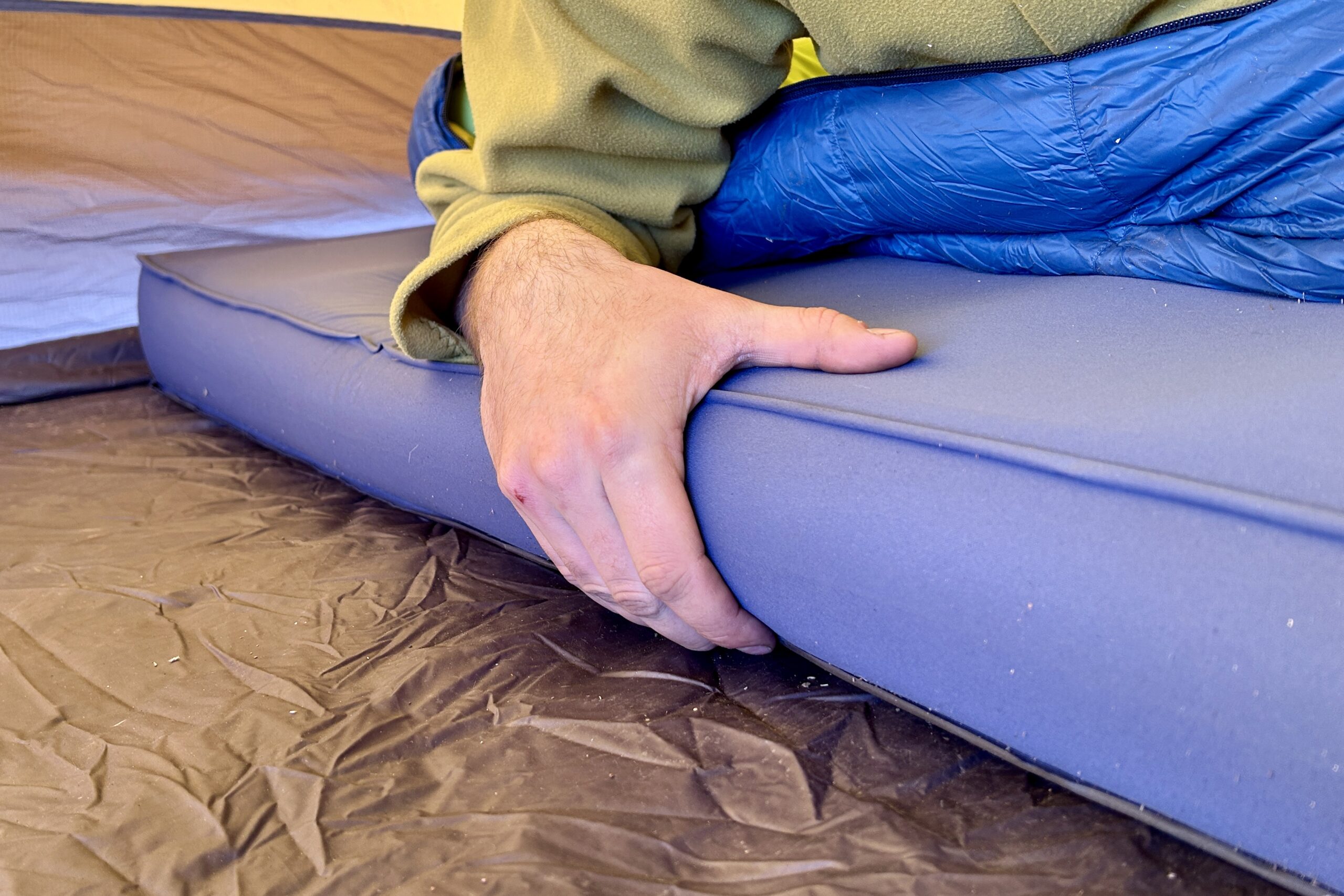 Close-up image of a person's hand on the side of a thick camping mattress.