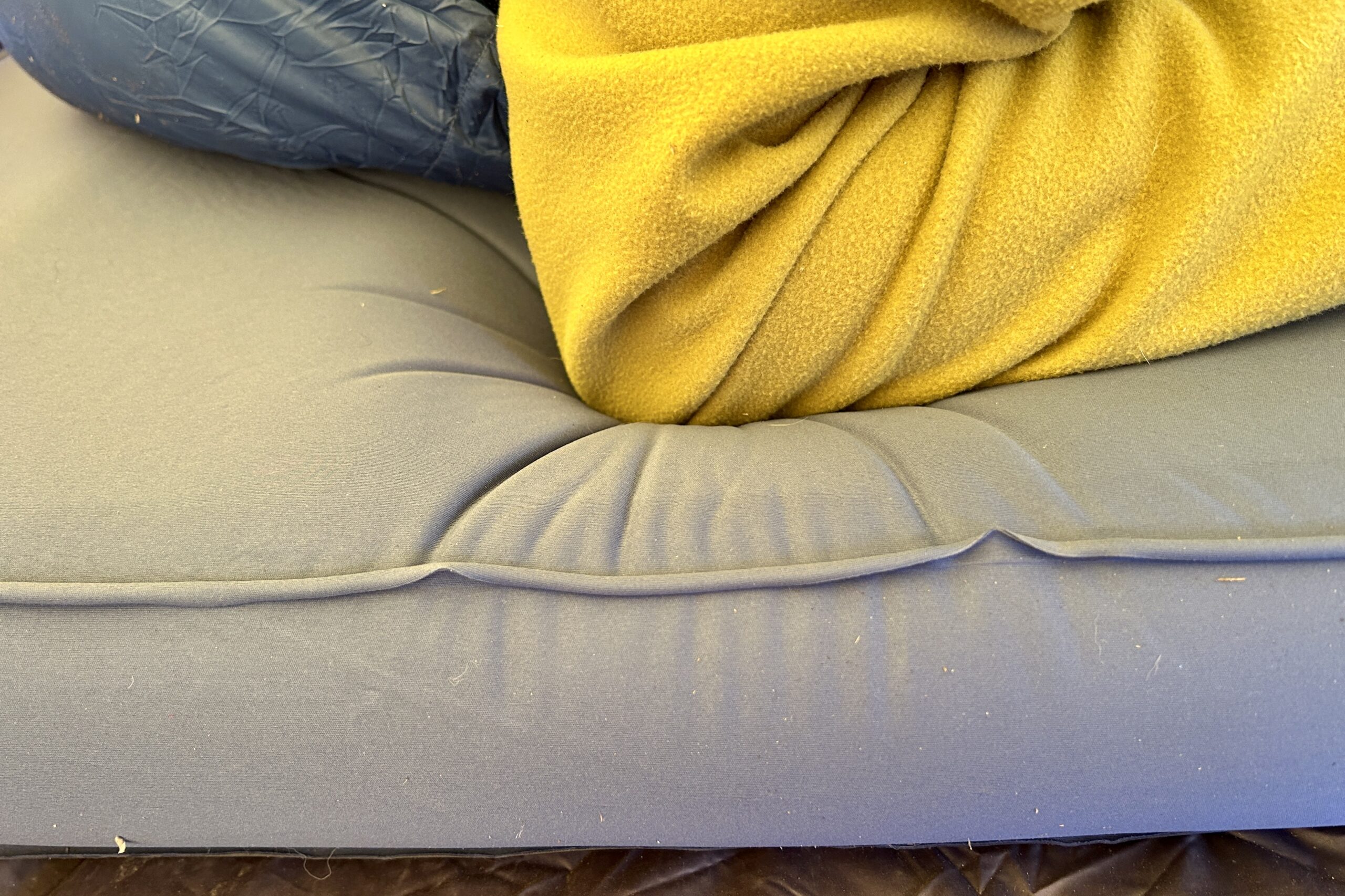 Close-up image of someon'es elbow pushing into a camping mattress. There are slight folds in the fabric from the pressure.
