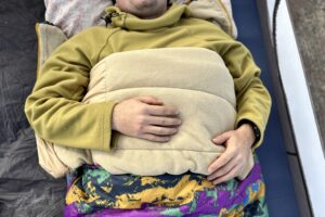 Close up image from above of a person laying in a sleeping bag with the edge folded down like a blanket, and their arms on top.