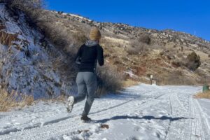 A hiker runs on snowy ground with a pair of ice cleats on a desert background.