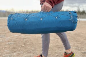 Close-up image of a person walking with a packaged camping mattress at their side.