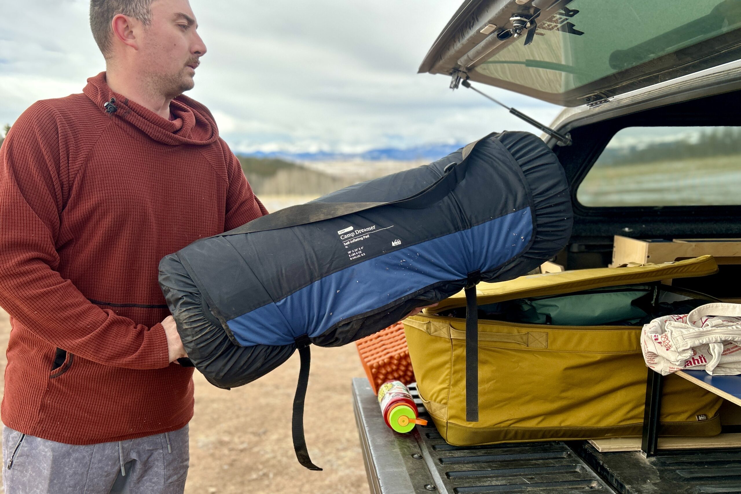 A man loads a rolled-up sleeping mattress into the back of a truck.