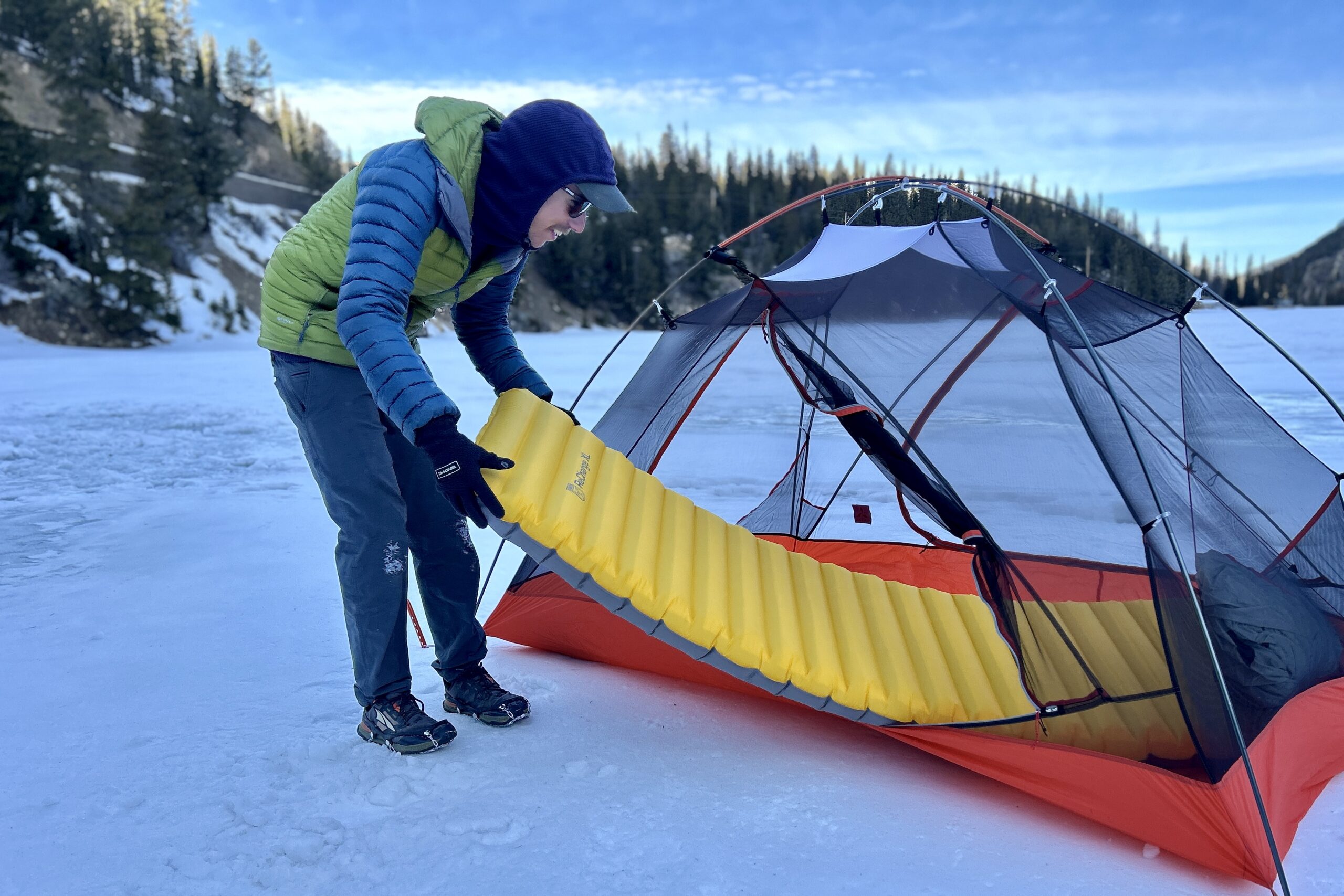 A man sets a sleeping pad inside of a tent in a snowy field.