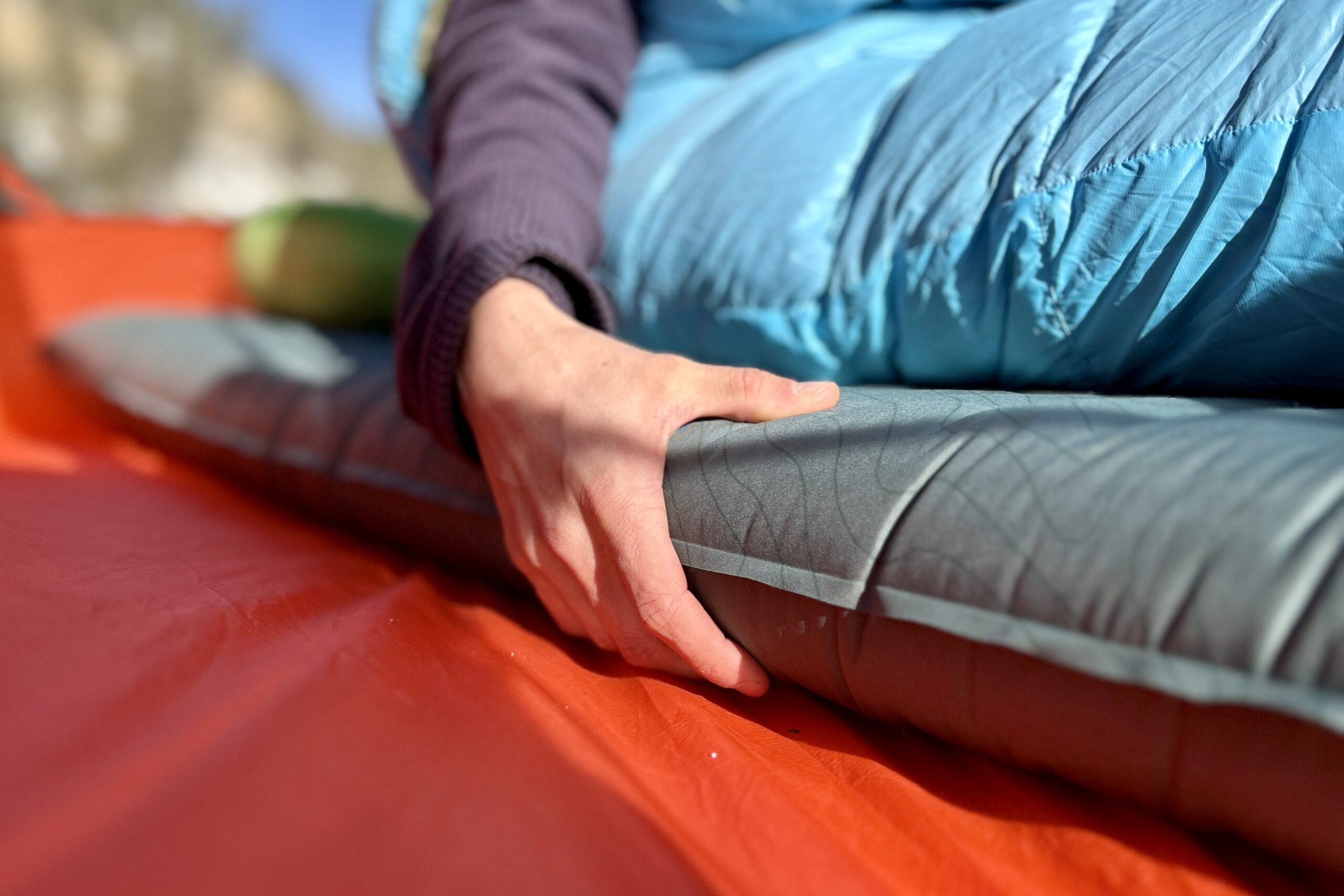 Close-up image of a person's hand holding onto the side of a sleeping pad.