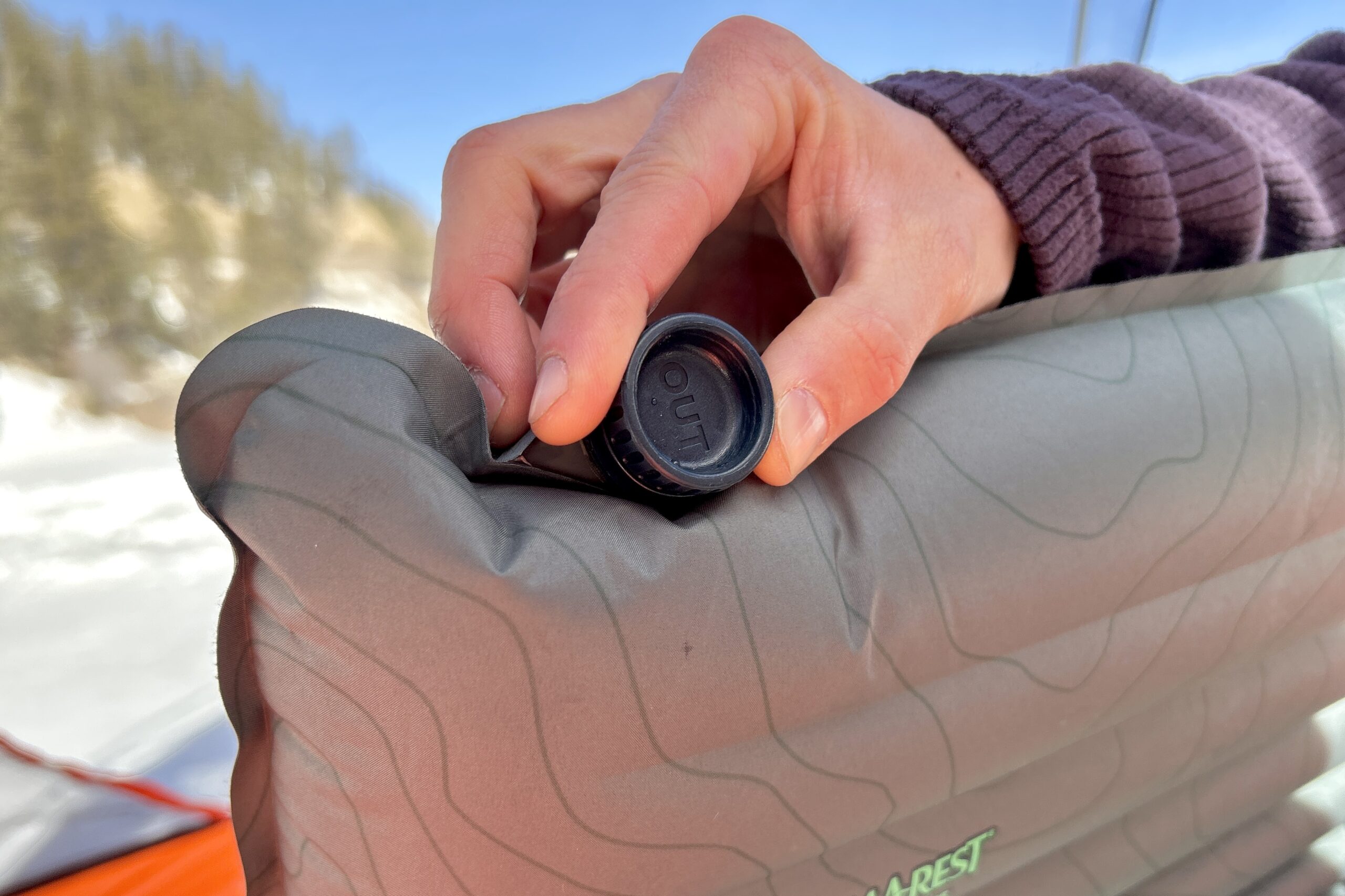Close-up image of a person adjusting the dump valve of a sleeping mattress.