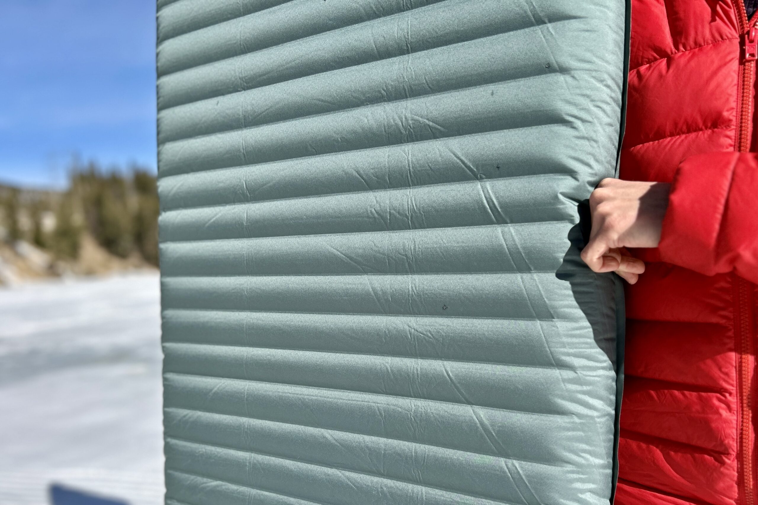 Close-up image of a person holding a sleeping bag with the smooth texture and narrow baffles visible.