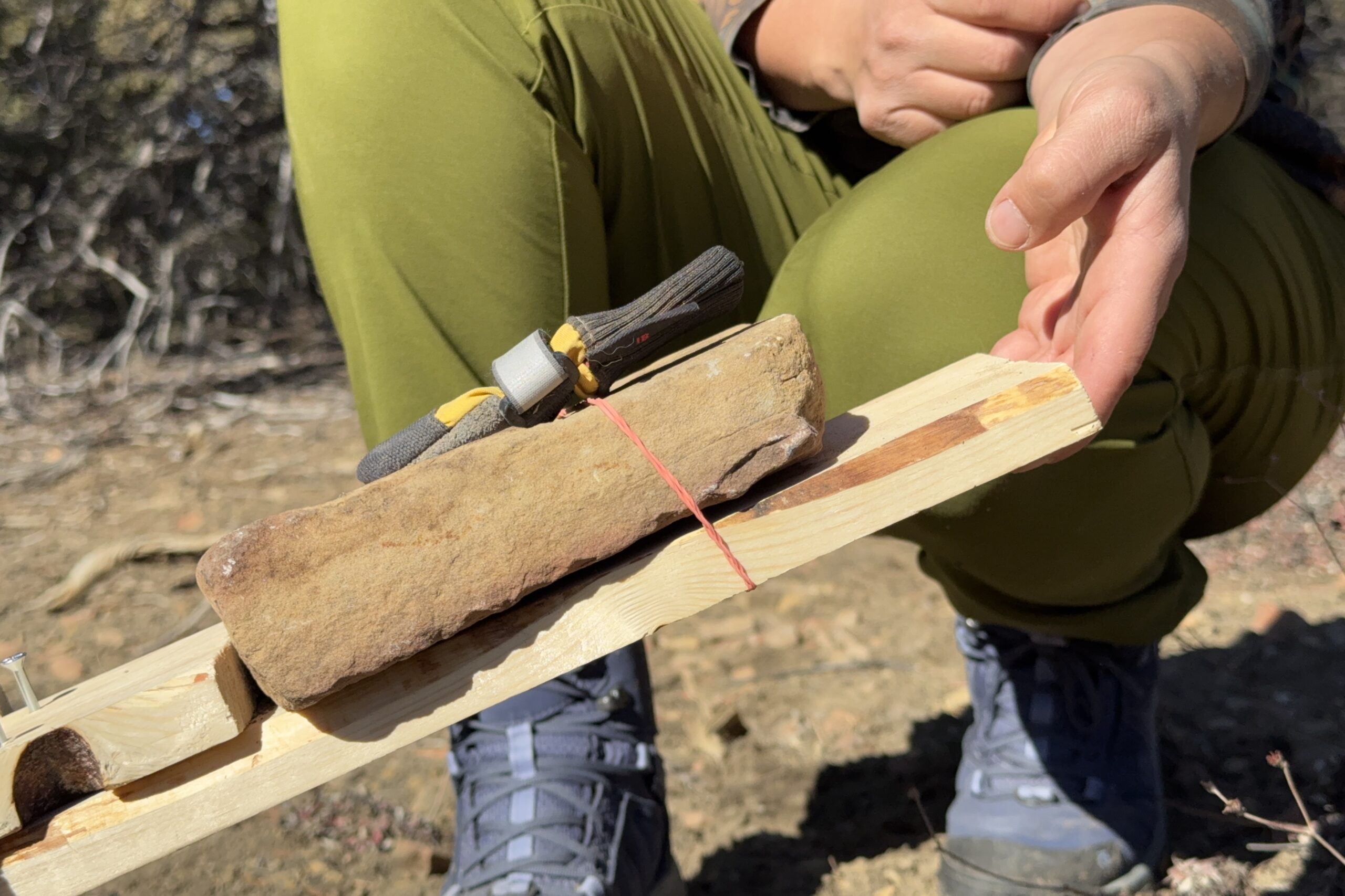 Close up picture of a Muttluks boot on the rock from the traction device. A hand is holding up the board that the rock balances on.