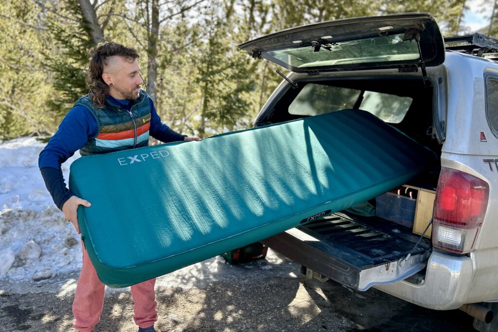 A man slides a large camping mattress into the back of a truck.