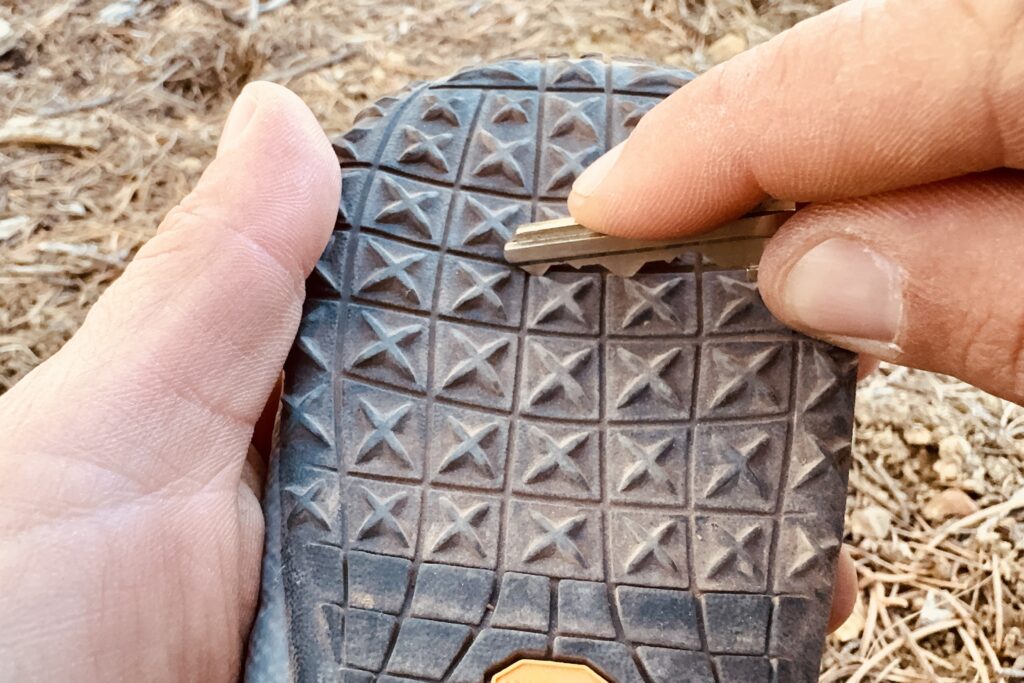 A close up of a hand scraping a Ruffwear boot with a house key.